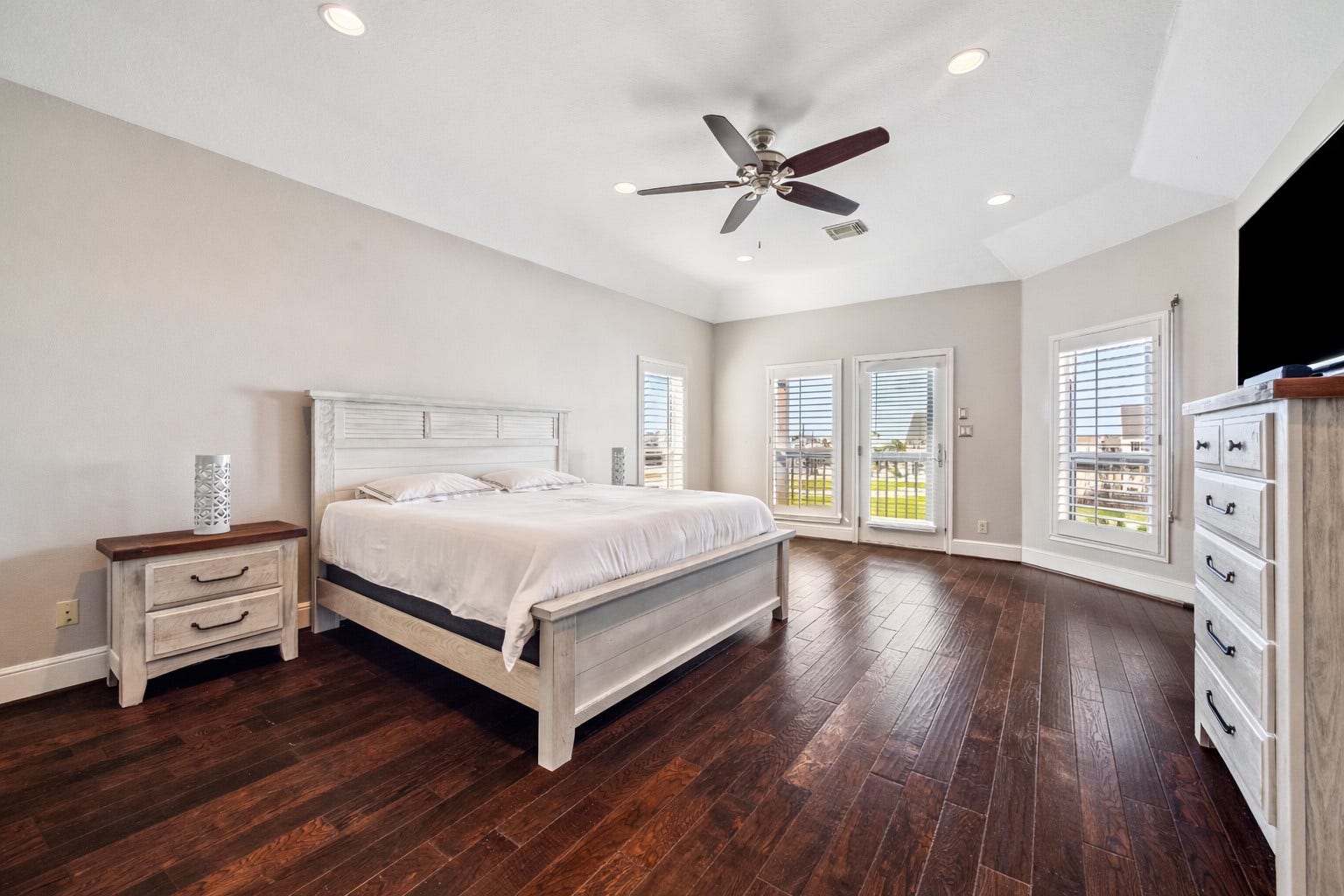 519 Westerly Drive, Tiki Island, TX 77554 Spacious bedroom with hardwood floors and ample natural light from multiple windows. Ceiling fan, neutral walls, and elegant furniture, offering a comfortable and inviting atmosphere.