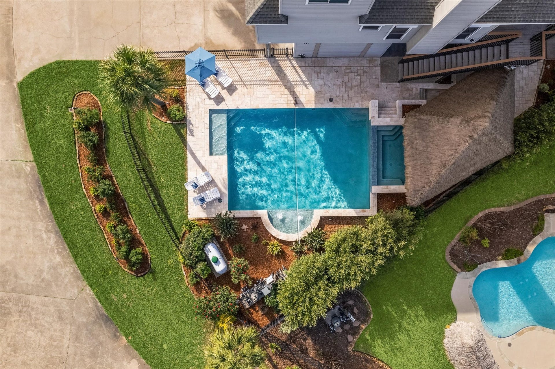 519 Westerly Drive, Tiki Island, TX 77554 This well-maintained backyard features a large rectangular pool with a spa, surrounded by a stone patio. There's a shaded area with seating and lush landscaping, creating an inviting space for relaxation and entertainment.