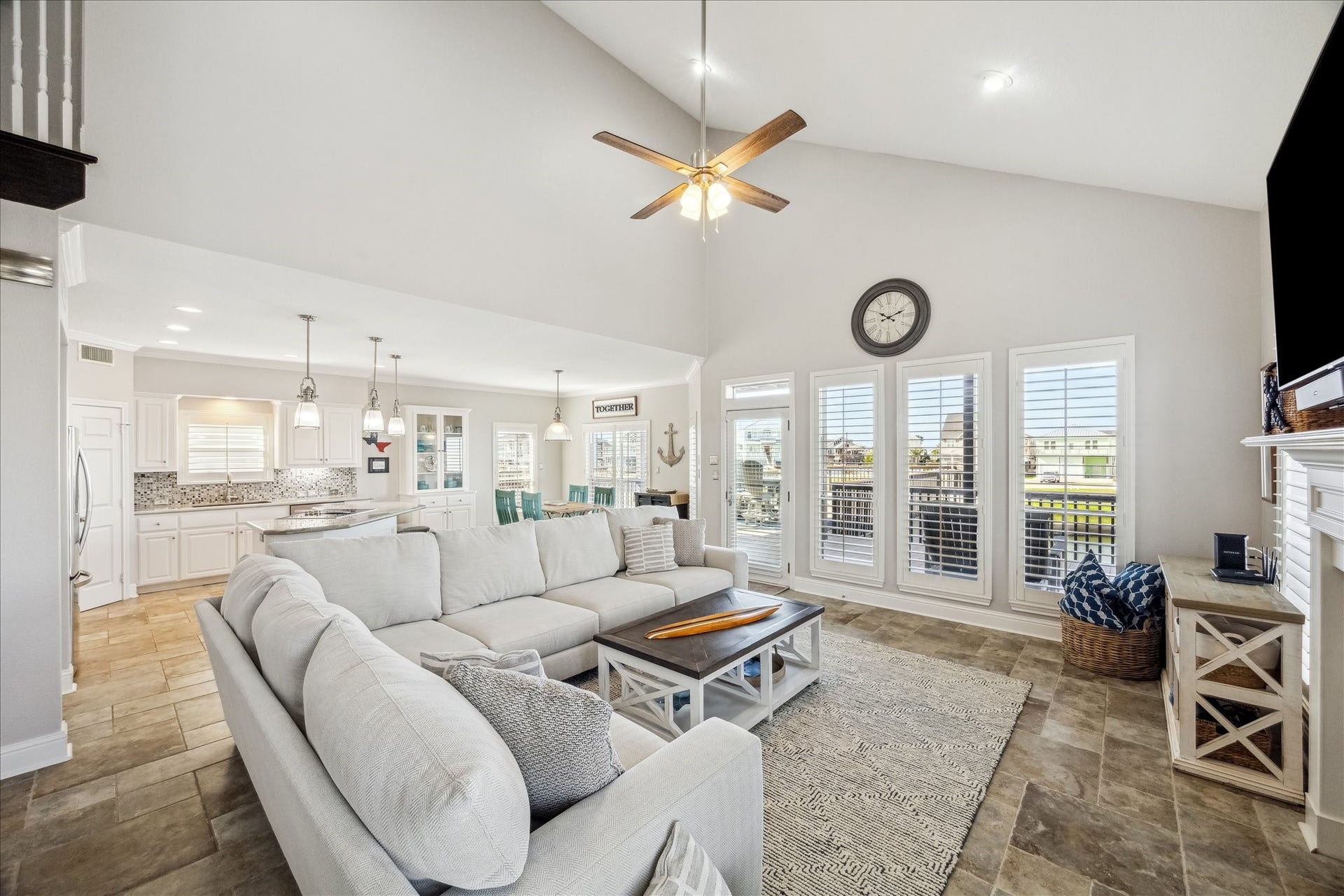 519 Westerly Drive, Tiki Island, TX 77554 This spacious living area features high ceilings, abundant natural light from large windows, and an open layout leading to a modern kitchen. The cozy seating area is complemented by neutral tones and a fireplace, creating a welcoming atmosphere ideal for family gatherings.