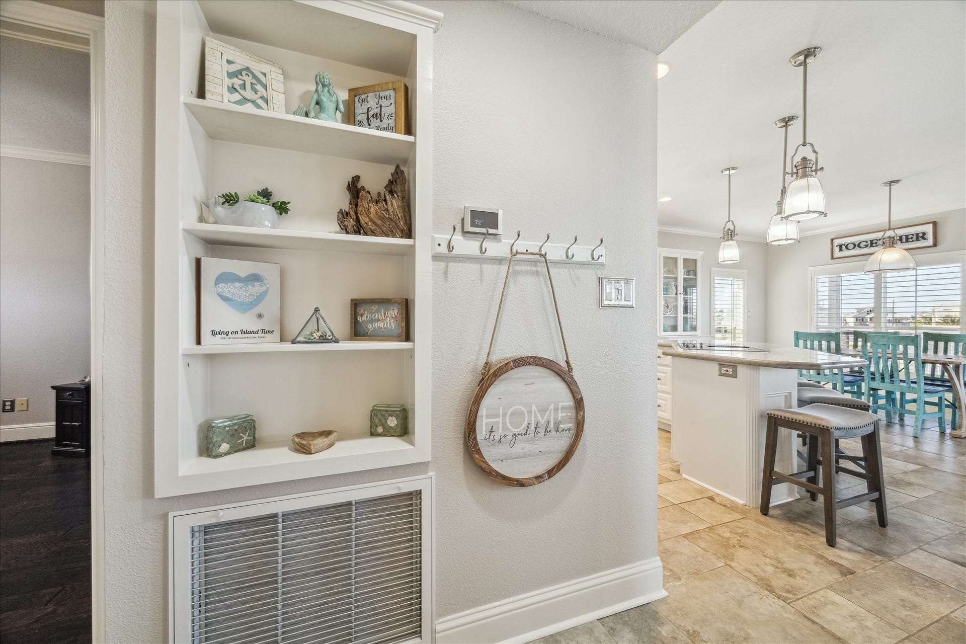 519 Westerly Drive, Tiki Island, TX 77554 Bright, inviting interior with built-in shelving and decorative accents. The open layout leads to a stylish kitchen with pendant lighting, an island with seating, and a dining area with large windows. The space is modern and welcoming.