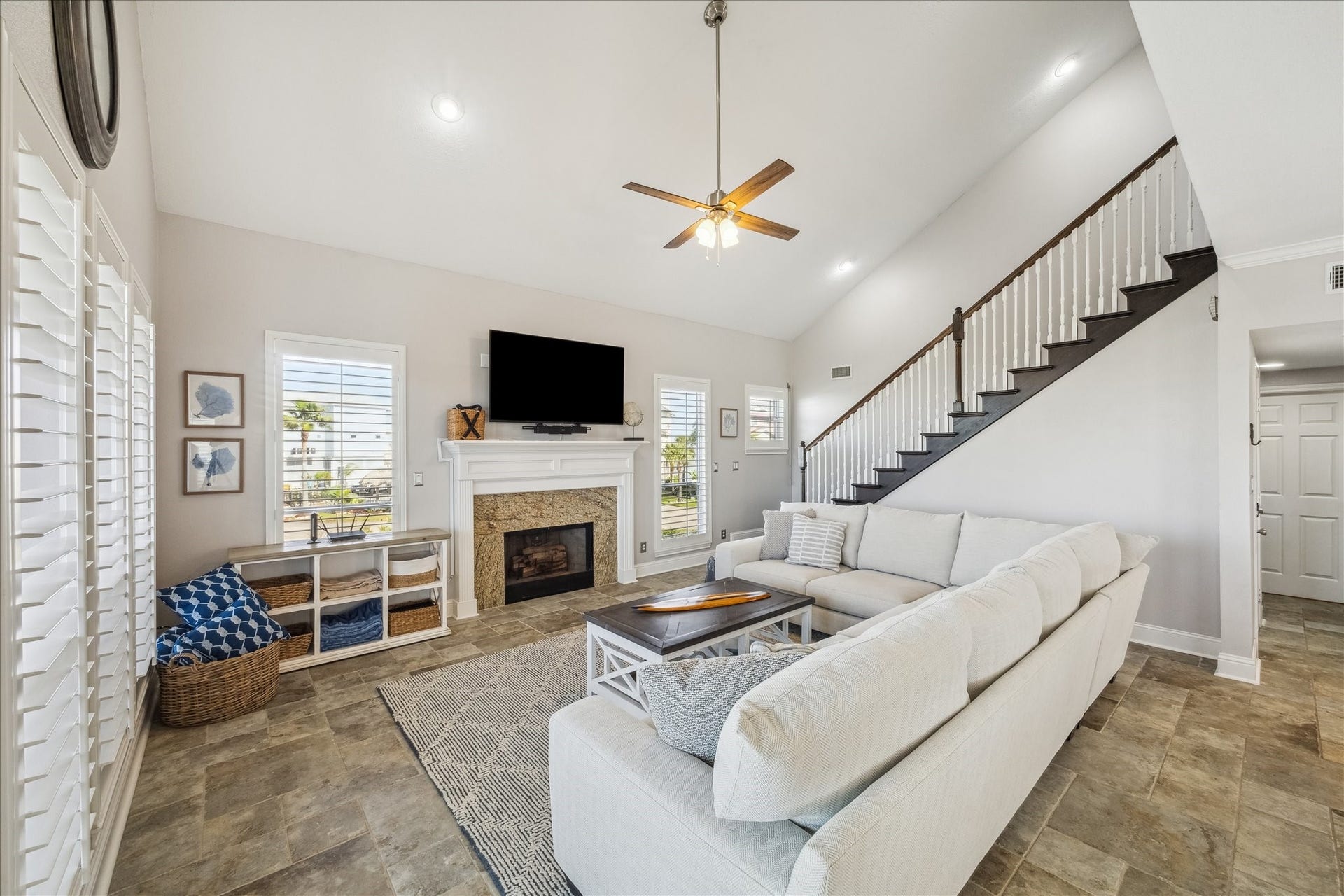 519 Westerly Drive, Tiki Island, TX 77554 Bright and spacious living room with high ceilings, featuring a cozy fireplace, large sectional sofa, and a mounted TV. The room is well-lit with natural light from multiple windows, and a staircase leads to the upper level, enhancing the open feel.