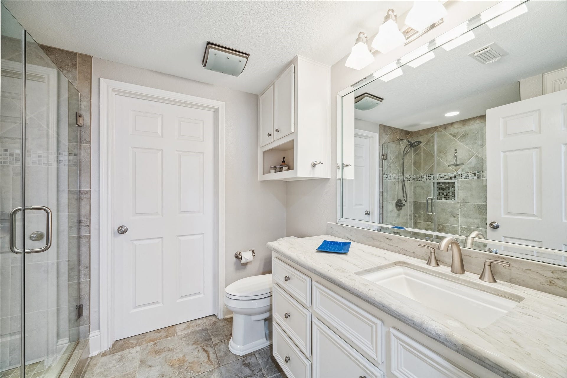 519 Westerly Drive, Tiki Island, TX 77554 This secondary bathroom features a modern design with a large glass-enclosed shower, elegant tile work, a marble countertop with dual sinks, and ample cabinet storage. Bright lighting and neutral tones create a fresh and inviting atmosphere.