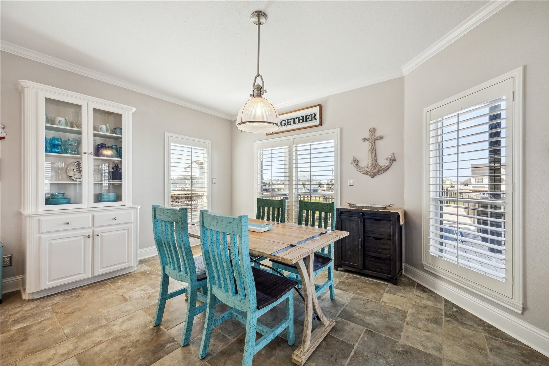519 Westerly Drive, Tiki Island, TX 77554 Bright dining area with a coastal vibe, featuring a wooden table, turquoise chairs, and a white cabinet. Large windows with shutters allow ample natural light, while nautical decor adds charm. Perfect for casual dining and entertaining.