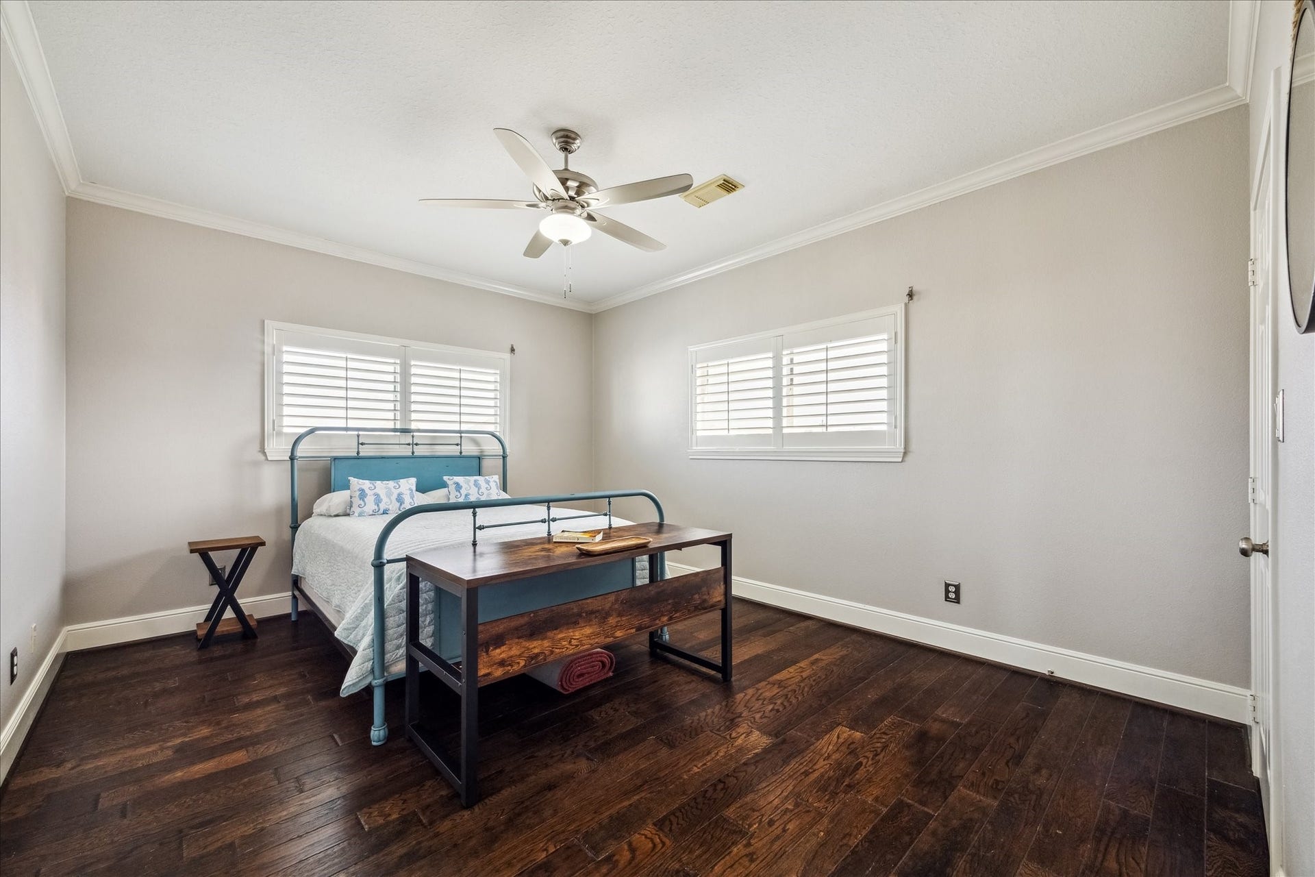 519 Westerly Drive, Tiki Island, TX 77554 This secondary bright bedroom features hardwood floors, neutral walls, and a ceiling fan. It includes a bed with a wooden bench at the foot and ample natural light from two windows with plantation shutters. The closet could be converted to a 3rd bath , plumbing is accessible.