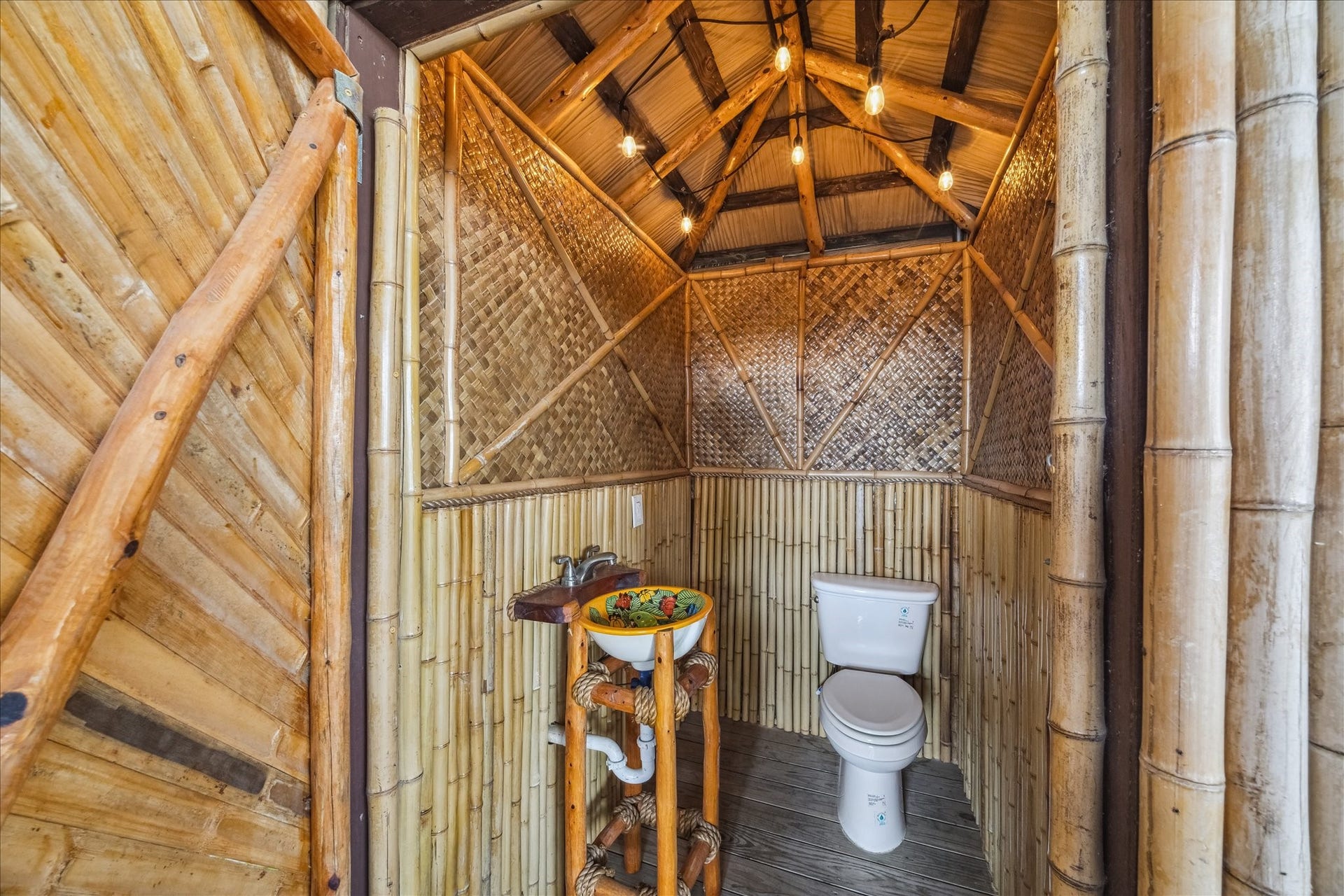 519 Westerly Drive, Tiki Island, TX 77554 This is a unique, rustic bathroom featuring bamboo walls and ceiling, with a colorful, artistic sink and modern toilet. Warm lighting adds a cozy ambiance, perfect for a tropical or nature-inspired home. Not permittable or insurable.