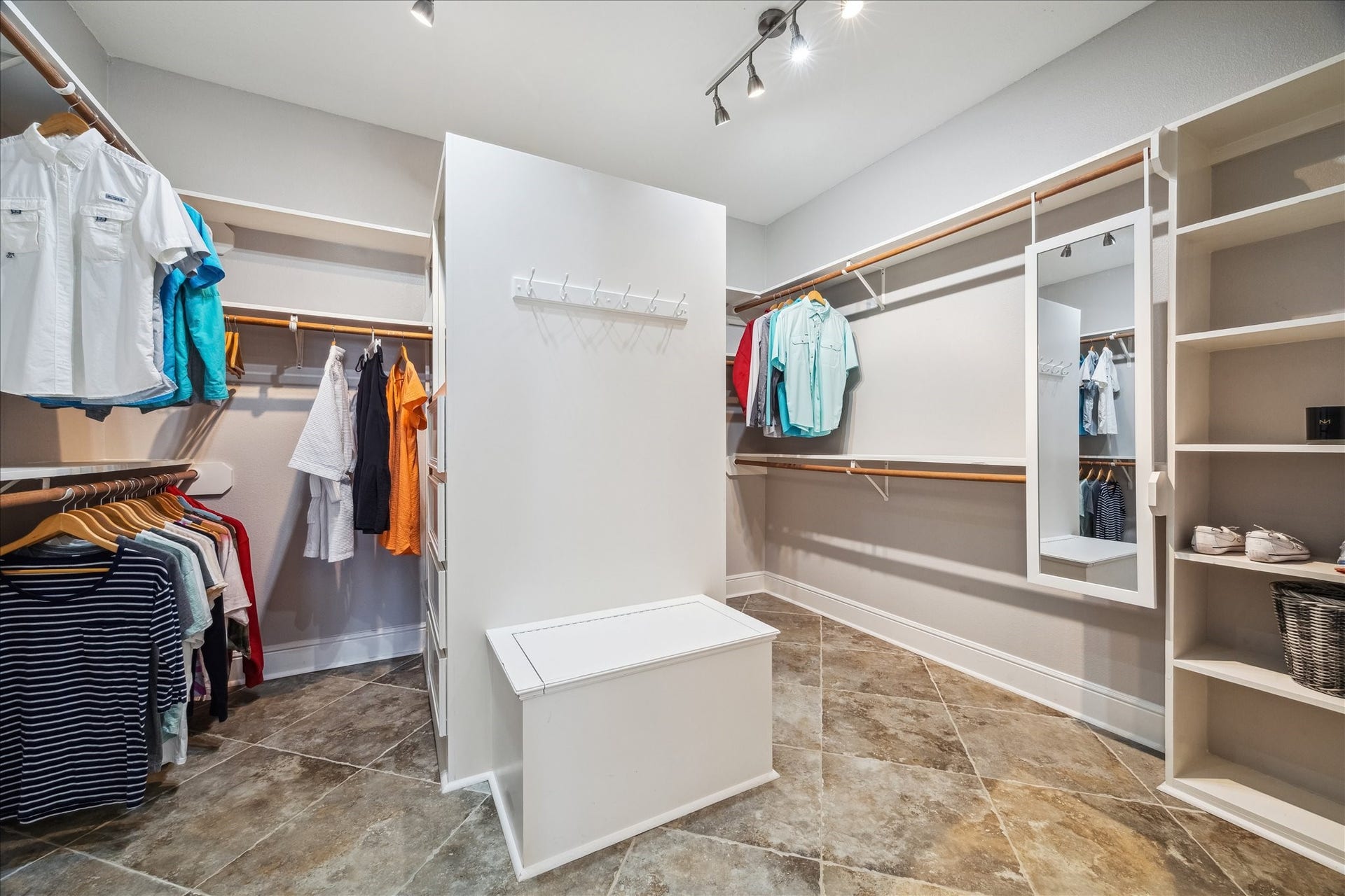 519 Westerly Drive, Tiki Island, TX 77554 This spacious walk-in closet features ample hanging space, built-in shelves, and a central island with seating. It's well-lit with modern track lighting and has tiled flooring for a sleek, functional look. Ideal for organizing and displaying your wardrobe.