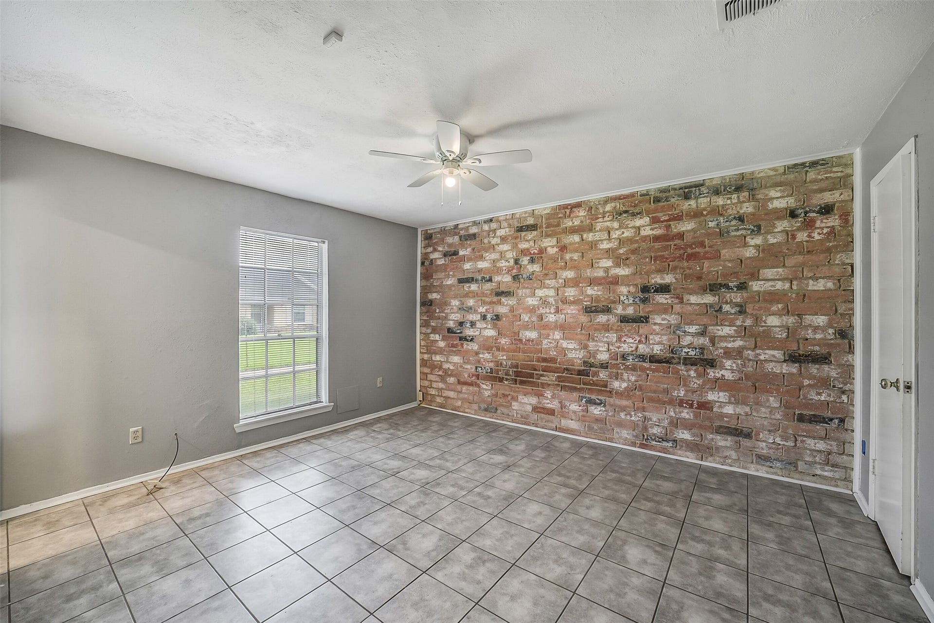 7265 Chasewood Drive, Houston, TX 77489 Retreat to the spacious primary suite featuring durable tile flooring, neutral paint, a ceiling fan, and an eye-catching exposed brick accent wall that adds warmth and character. A large window fills the room with natural light, creating a bright and relaxing owner's retreat.