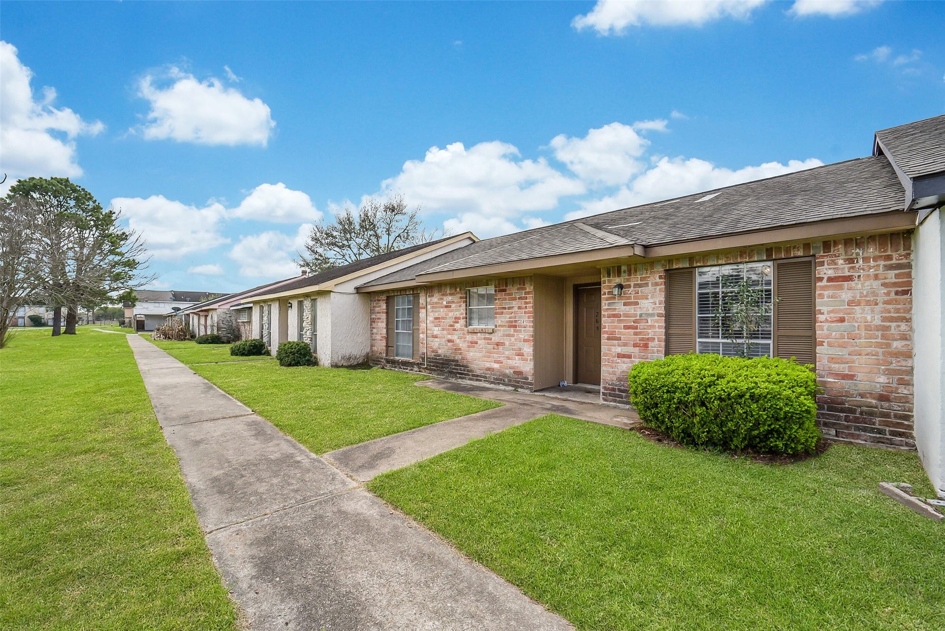 7265 Chasewood Drive, Houston, TX 77489 A second exterior perspective showcases the home's attractive brick exterior, covered front porch, and spacious greenbelt-style common area. Mature landscaping and wide sidewalks provide an open, park-like setting that enhances the neighborhood's welcoming feel.