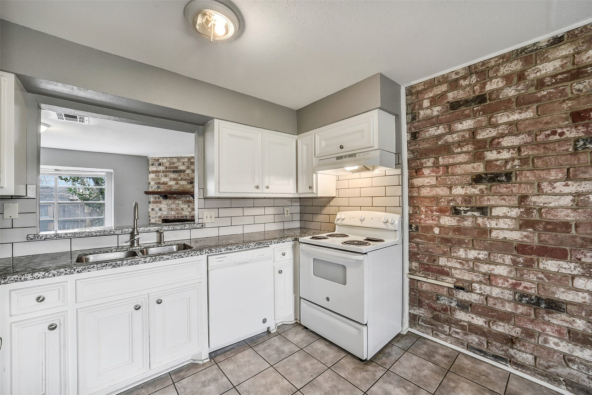 7265 Chasewood Drive, Houston, TX 77489 From this angle, the kitchen showcases generous cabinet storage, granite counters, updated hardware, and a convenient double-basin sink overlooking the living area. The exposed brick accent wall adds warmth and character while complementing the home's inviting design.