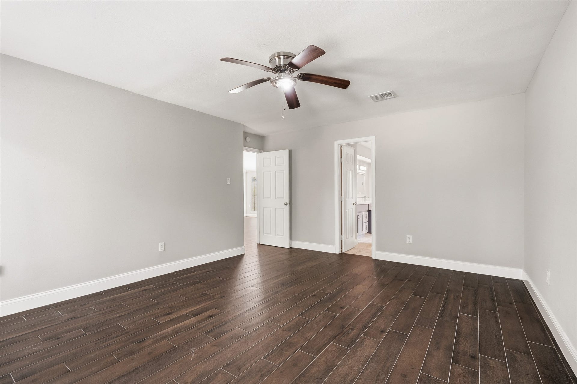 Spacious bedroom featuring neutral walls and a ceiling fan, leading to a bright ensuite bathroom.