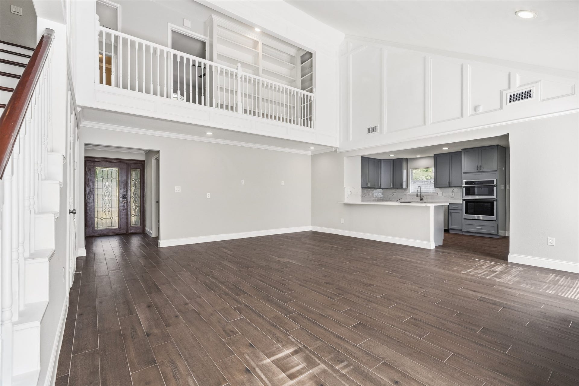 Spacious open-concept living area with elegant dark flooring, a high ceiling, and a modern kitchen featuring sleek gray cabinetry and stainless steel appliances.