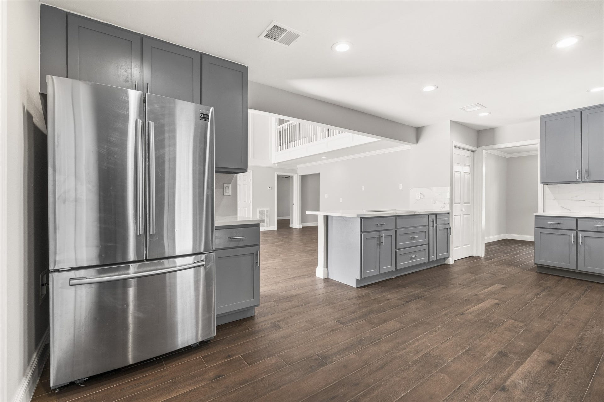 Spacious kitchen featuring sleek stainless steel appliances, elegant gray cabinetry, and dark flooring, seamlessly connecting to a bright, open living area.
