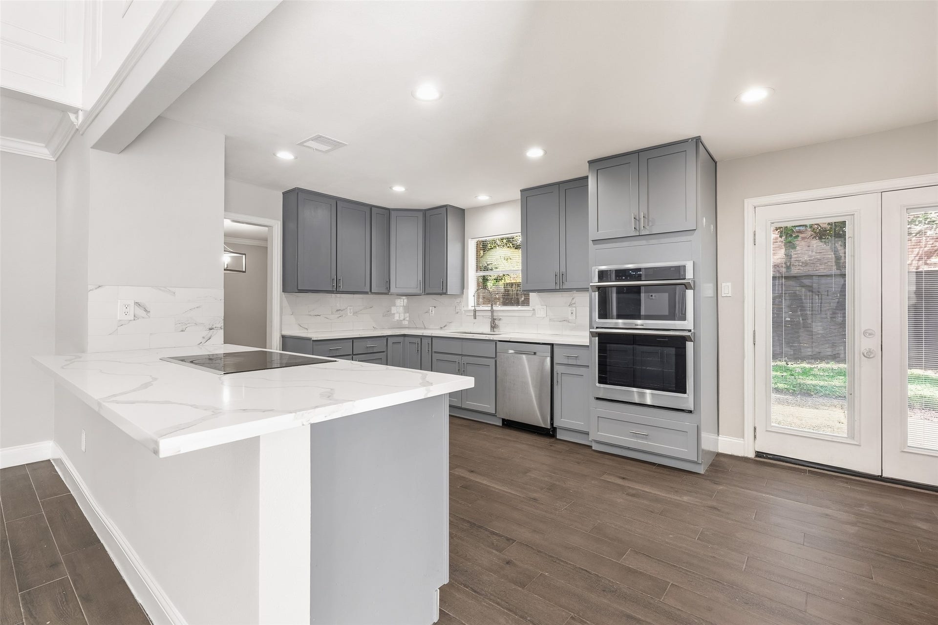 Modern kitchen with sleek gray cabinetry, stainless steel appliances, and modern countertops, complemented by abundant natural light.