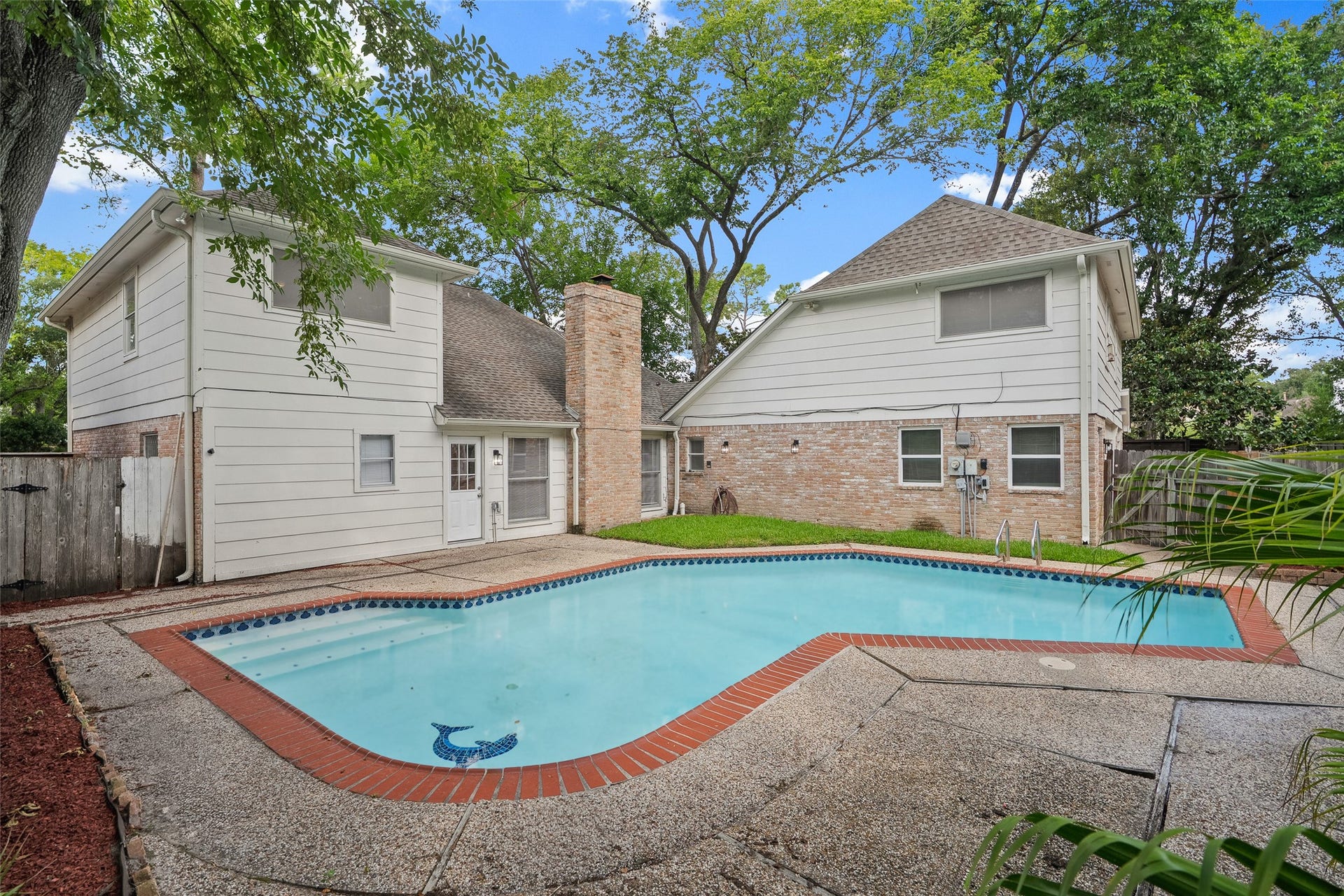 Charming backyard oasis featuring a sparkling pool surrounded by mature trees and a spacious deck, perfect for relaxation and entertaining.