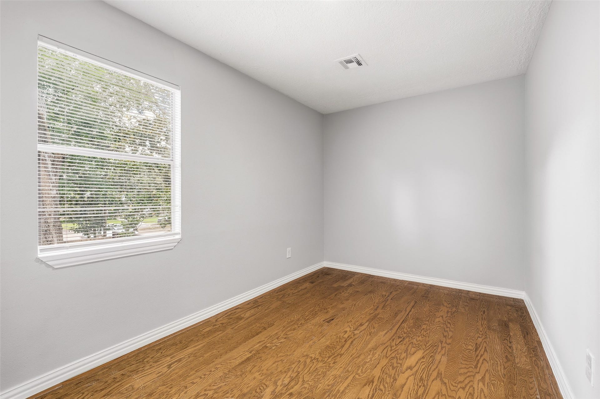 Bright and inviting room with fresh neutral walls, rich hardwood floors, and a large window offering plenty of natural light.