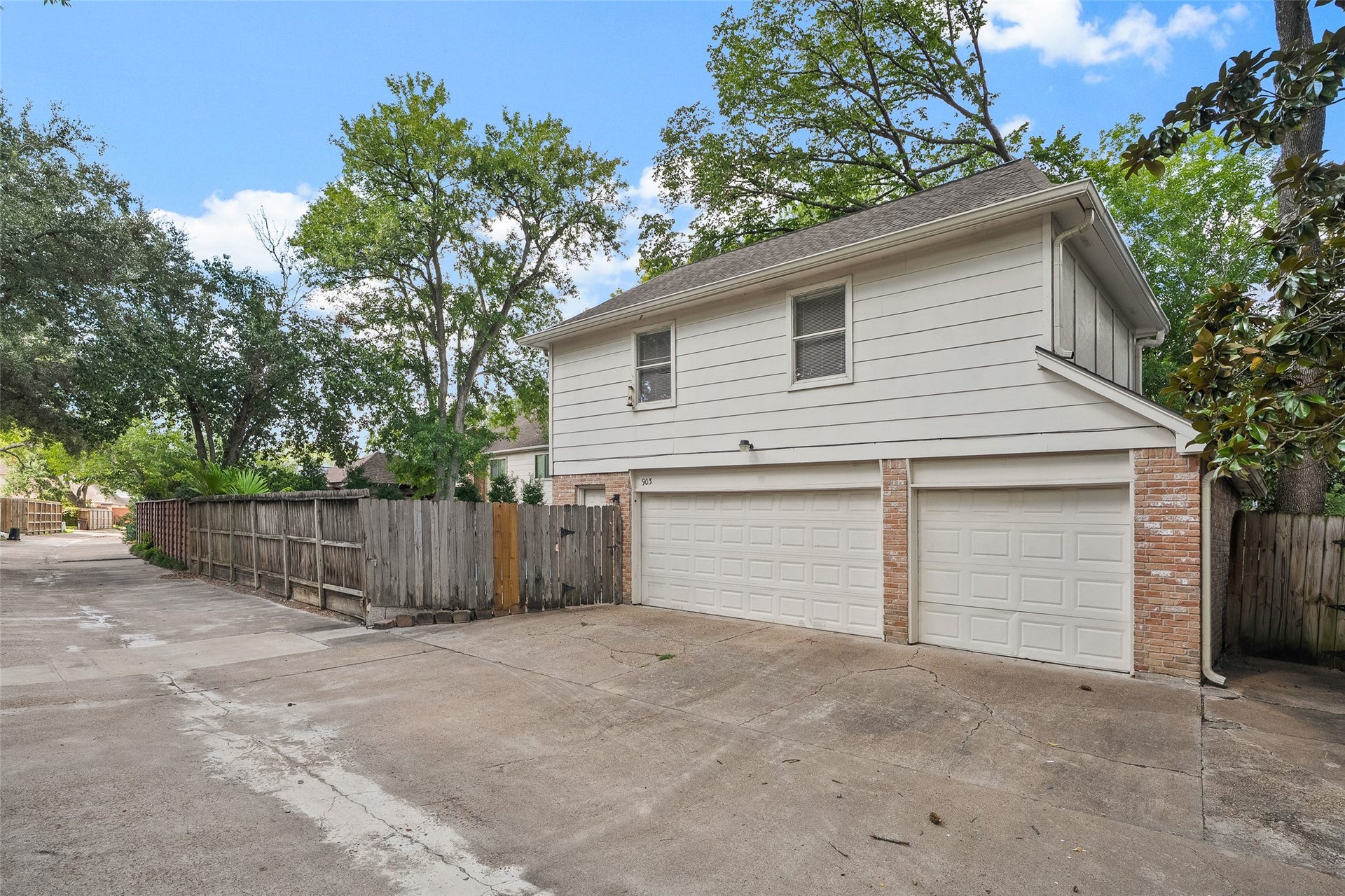 Spacious three-car garage with a private driveway, framed by mature trees and a wooden fence, offering ample parking and storage.
