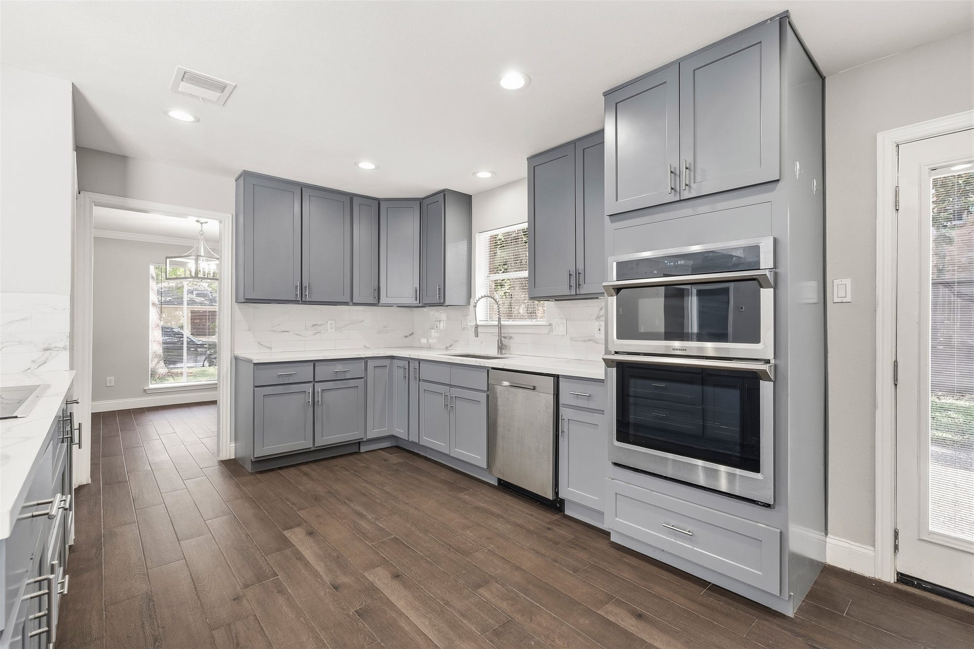 Sleek kitchen featuring elegant gray cabinetry, stainless steel appliances, and dark flooring, all bathed in abundant natural light.