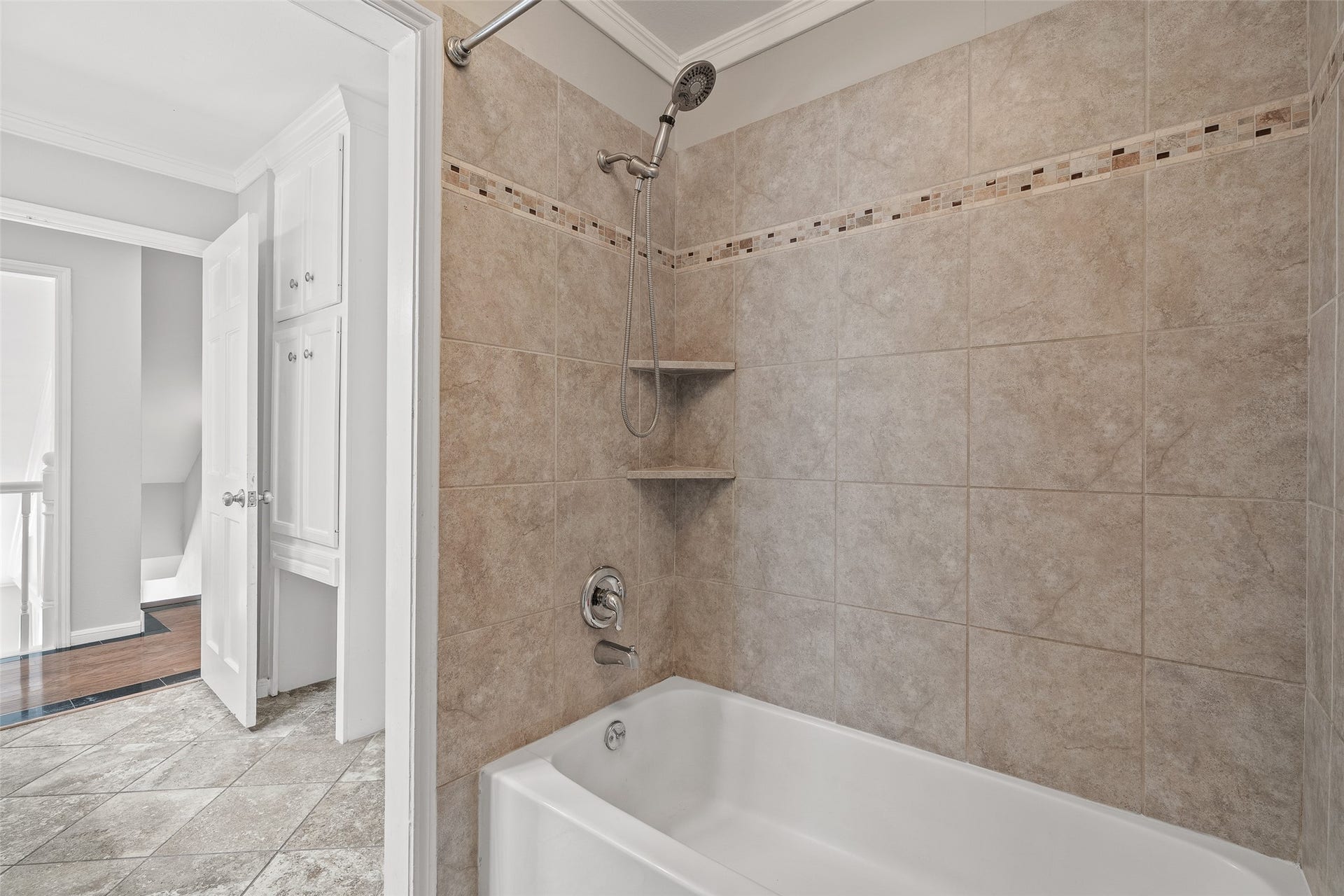 Elegant bathroom featuring a tiled shower-bathtub combo with built-in shelves and modern fixtures, complemented by stylish flooring and convenient hallway access.