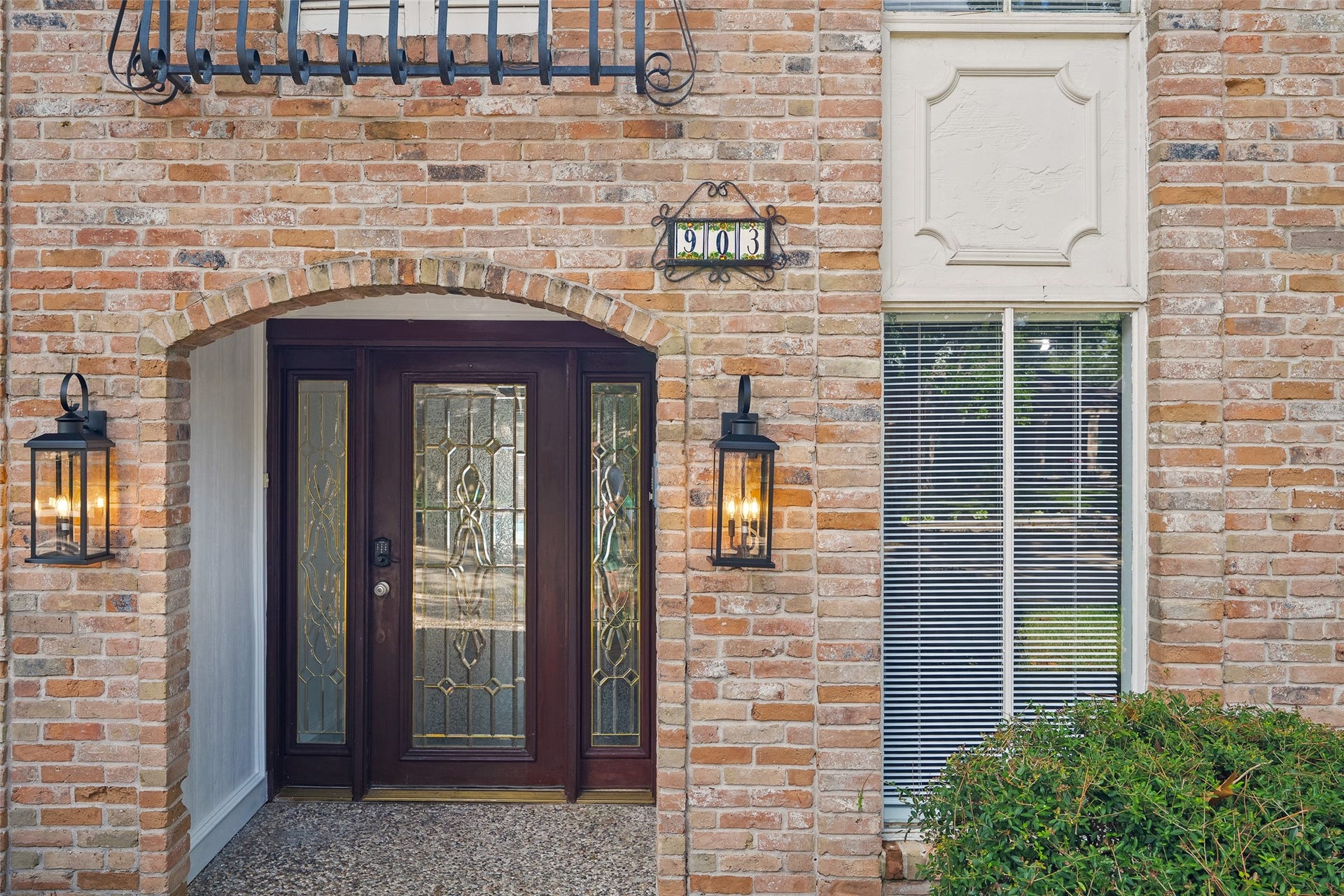 Charming entrance featuring a brick archway, decorative glass door, elegant lantern lighting, and classic window accents, offering a warm welcome.