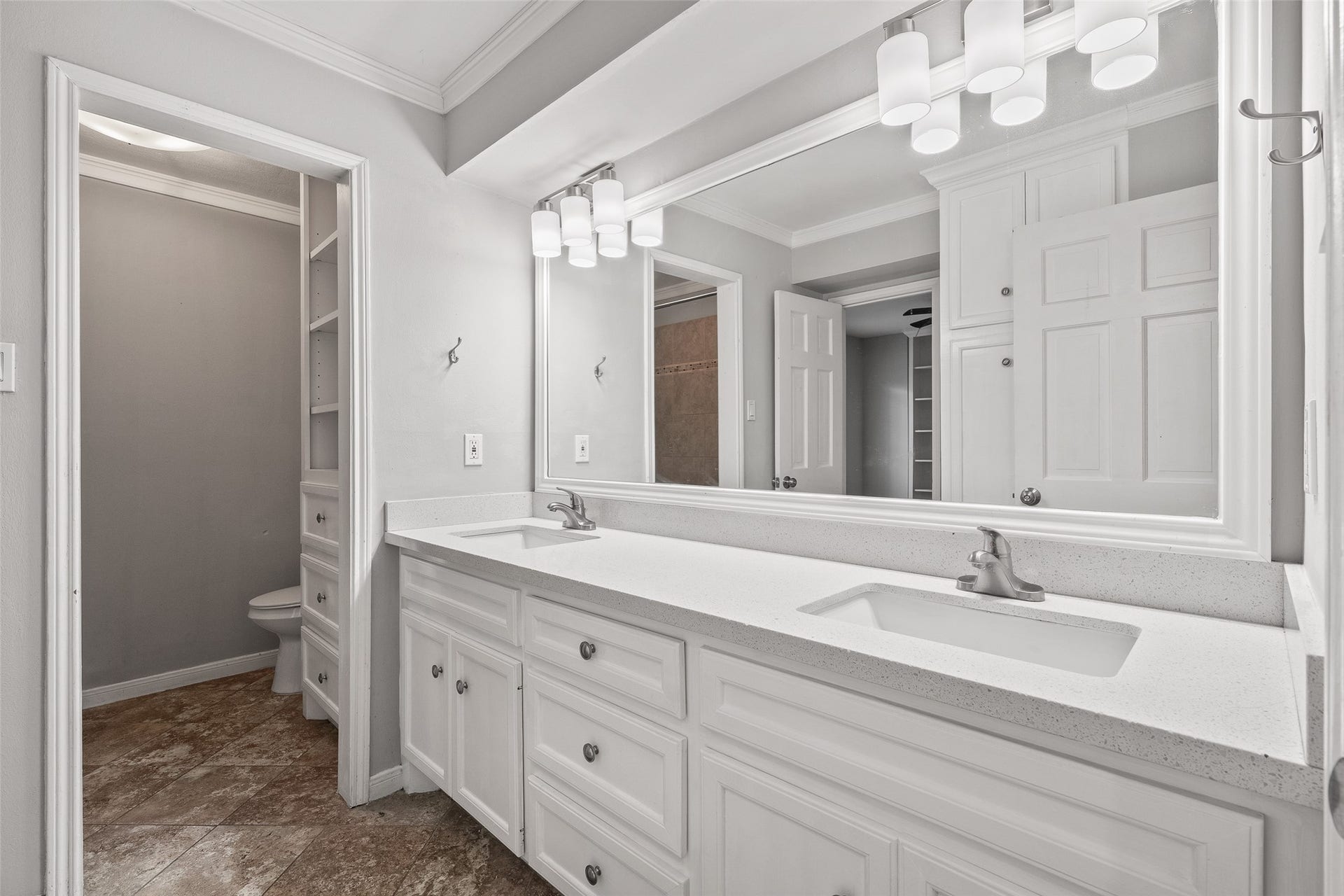Elegant bathroom featuring a dual-sink vanity with sleek countertops, ample storage, and modern lighting, complemented by neutral tones and tile flooring.