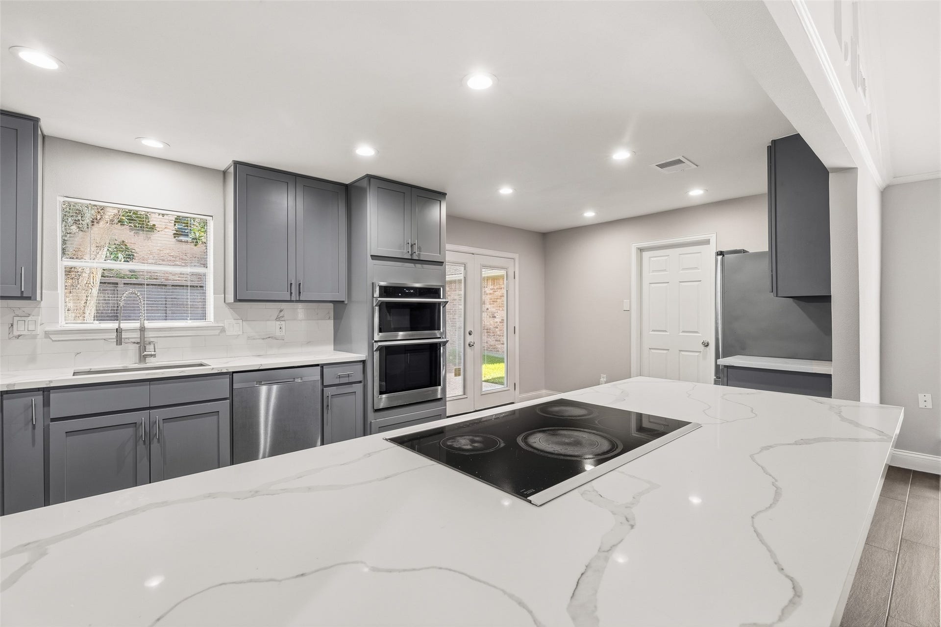 Modern kitchen with sleek gray cabinetry and stainless steel appliances. Bright and inviting with natural light from large windows and a glass door leading to the backyard.