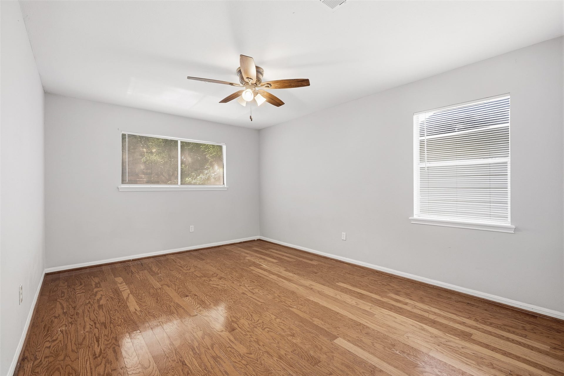 Bright and spacious bedroom featuring elegant flooring, abundant natural light, and a ceiling fan for added comfort.