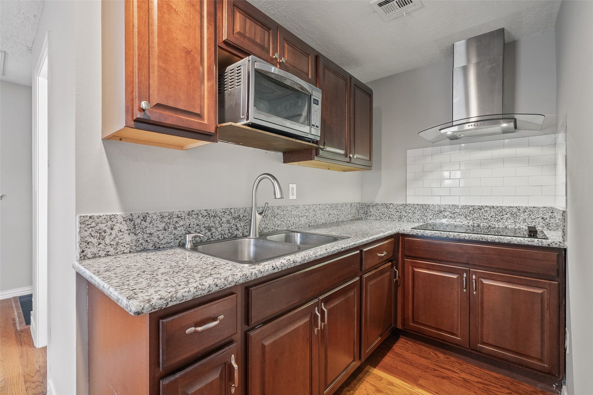 Modern kitchen with elegant countertops, rich  cabinetry, and stainless steel appliances, including a sleek range hood and built-in microwave.