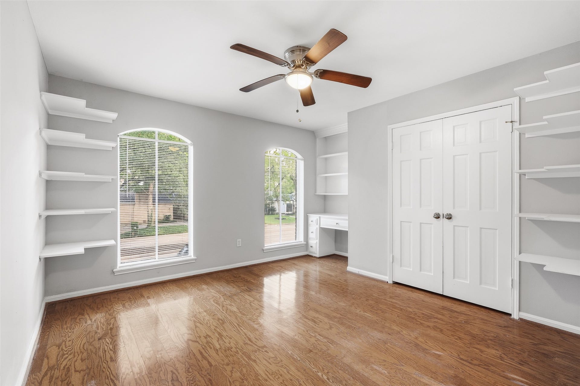 Bright and airy room featuring built-in shelving, large arched windows, and a ceiling fan, perfect for a home office or cozy retreat.
