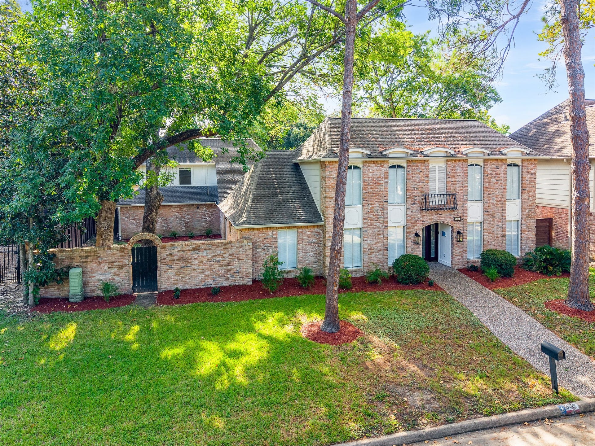 Elegant two-story brick home with a charming arched entryway, surrounded by mature trees and lush greenery, offering a welcoming and private atmosphere.