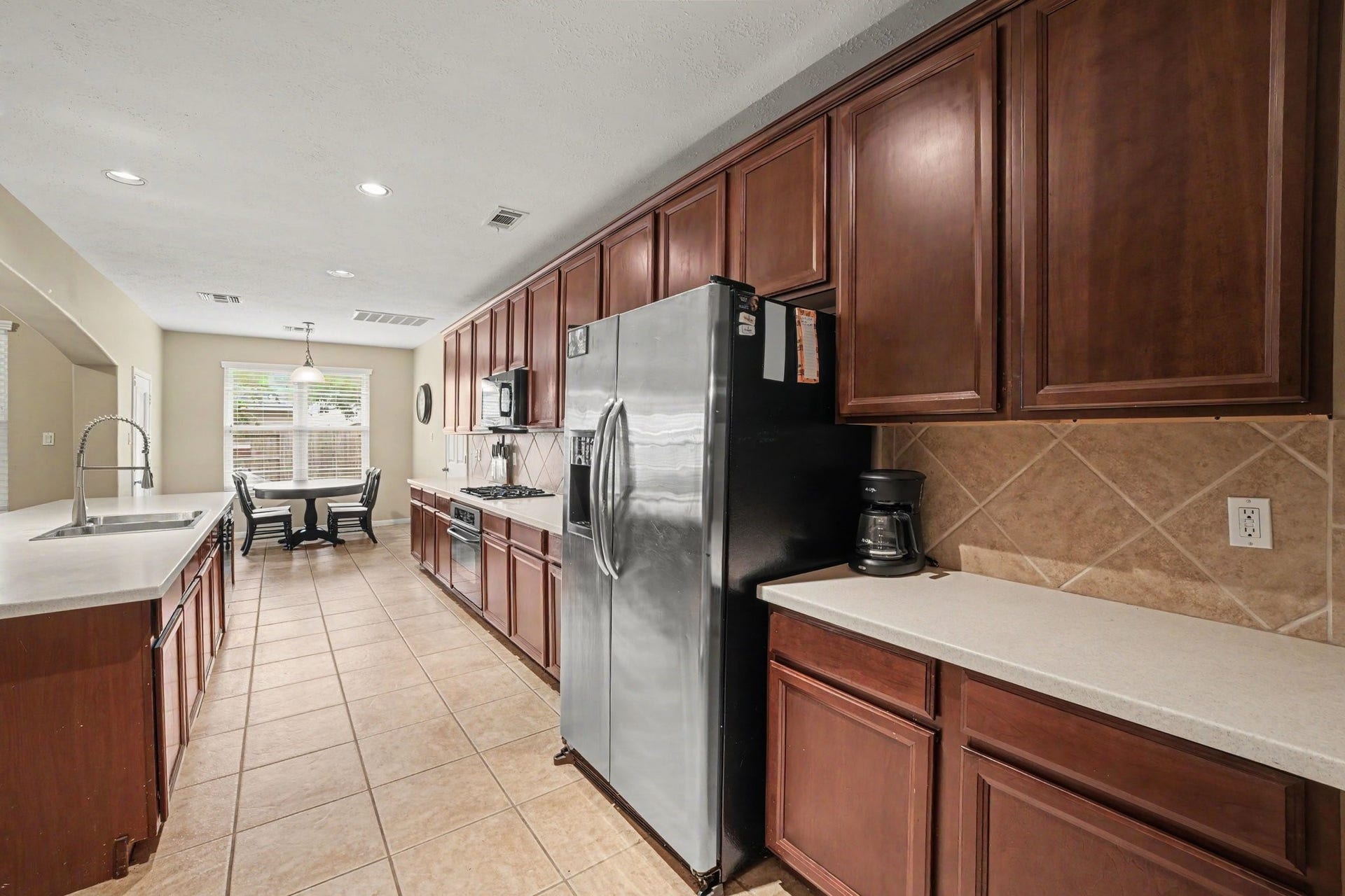12807 Rocky Briar Lane, Tomball, TX 77377 Another view of the kitchen showcases the abundant rich wood cabinetry, stainless steel appliances, tile backsplash, and ample counter space, with a charming breakfast nook overlooking the backyard.