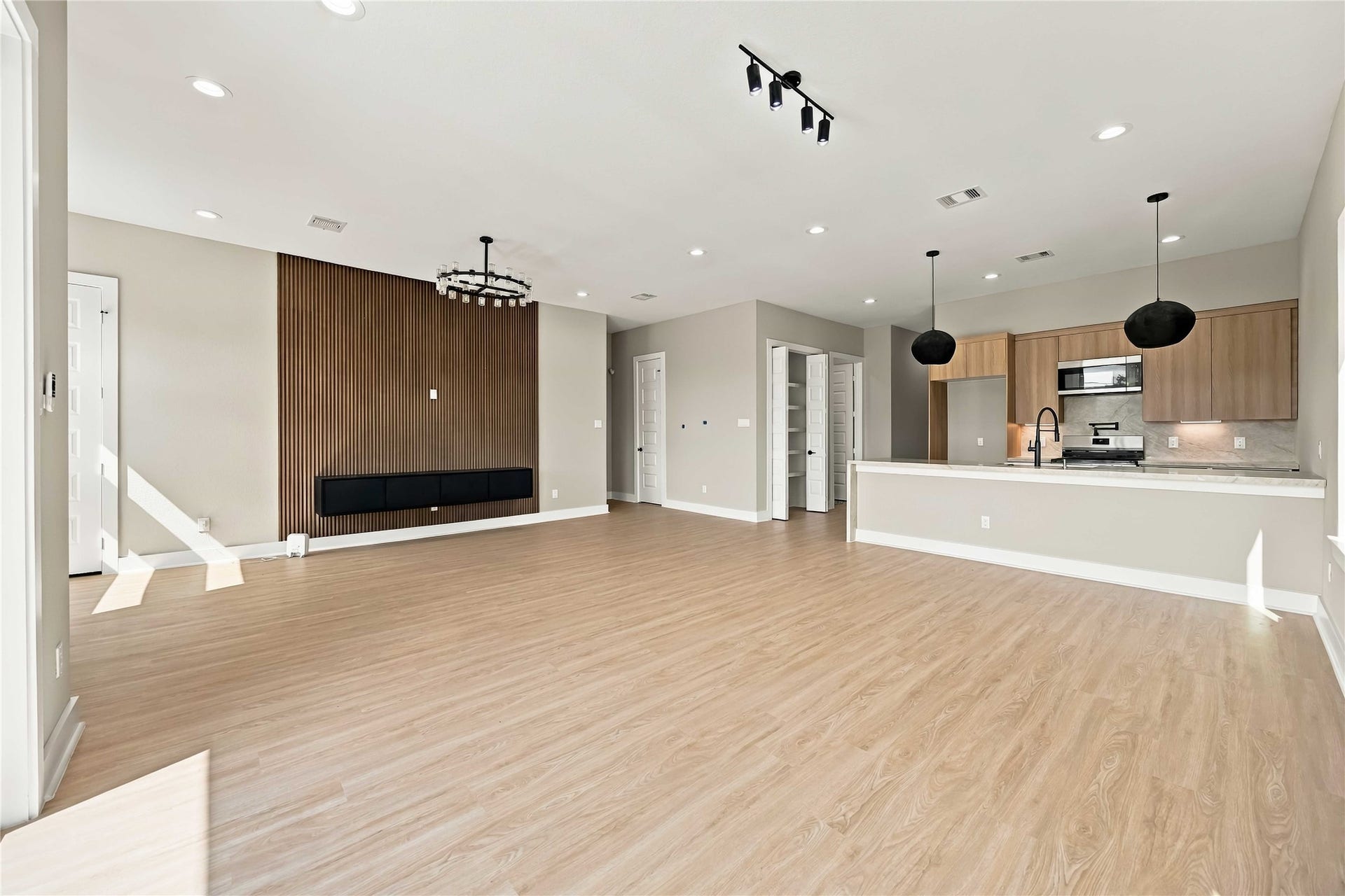 3503 Rebecca Street, #E/F, Houston, TX 77021 Open-concept living area featuring warm wood-look flooring, floating entertainment mantel, a striking vertical wood-slat accent wall, contemporary designer lighting, and a clean, modern aesthetic. The bright, airy layout flows seamlessly into the kitchen, creating an inviting space ideal for everyday living and entertaining.