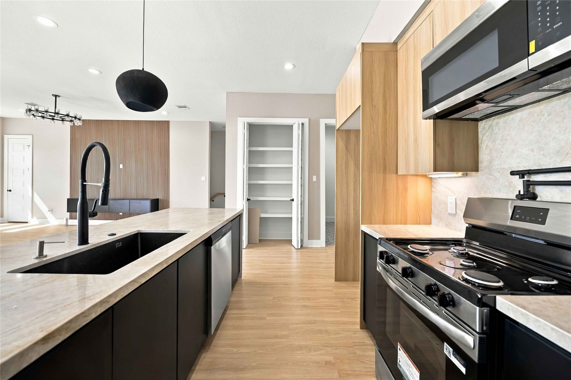 3503 Rebecca Street, #E/F, Houston, TX 77021 Sleek contemporary kitchen featuring warm natural wood cabinetry, contrasting black lower cabinets, elegant light stone countertops, a spacious island with a matte black gooseneck faucet, stainless steel appliances, and a modern backsplash. Recessed lighting and designer pendant fixtures complete this sophisticated, open-concept space.