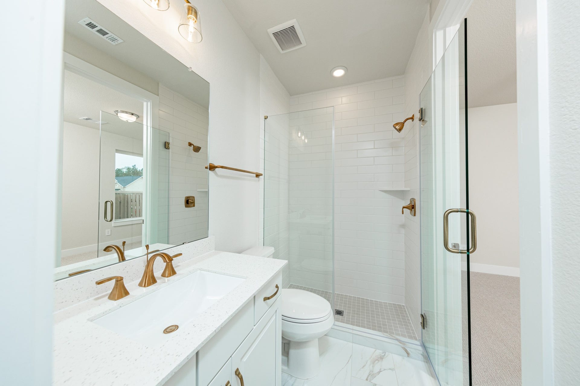 The private en suite bathroom features a modern white vanity with matte gold fixtures, mirror, lights, recessed lighting over the walk-in shower.