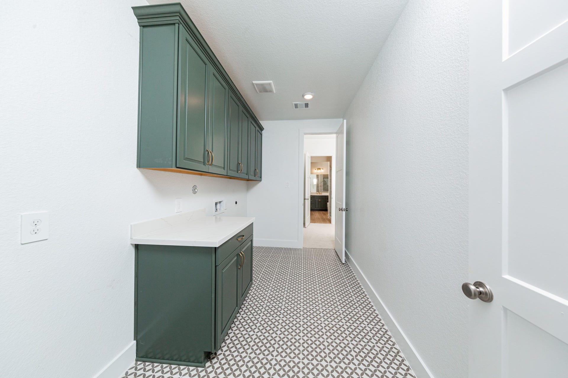 This bright and functional laundry room is conveniently located right off the primary walk-in closet and is ready for your appliances. It features clean white walls, trim, cabinets, and tile flooring.