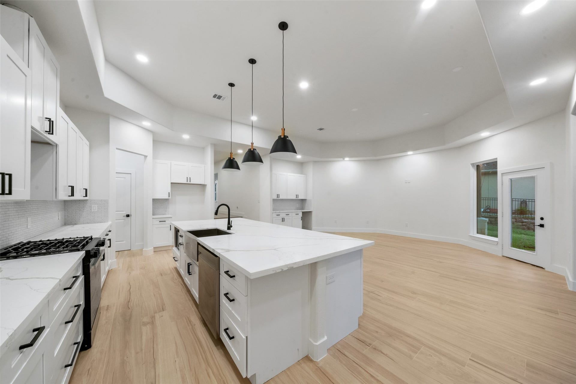 4833 W Fork Boulevard, Conroe, TX 77304 Beautifully designed gourmet kitchen featuring an oversized island with marble-look countertops, farmhouse-style sink, designer pendant lighting, and elegant white cabinetry with contrasting black hardware. The expansive open-concept layout flows effortlessly into the spacious living area, creating an exceptional setting for entertaining.