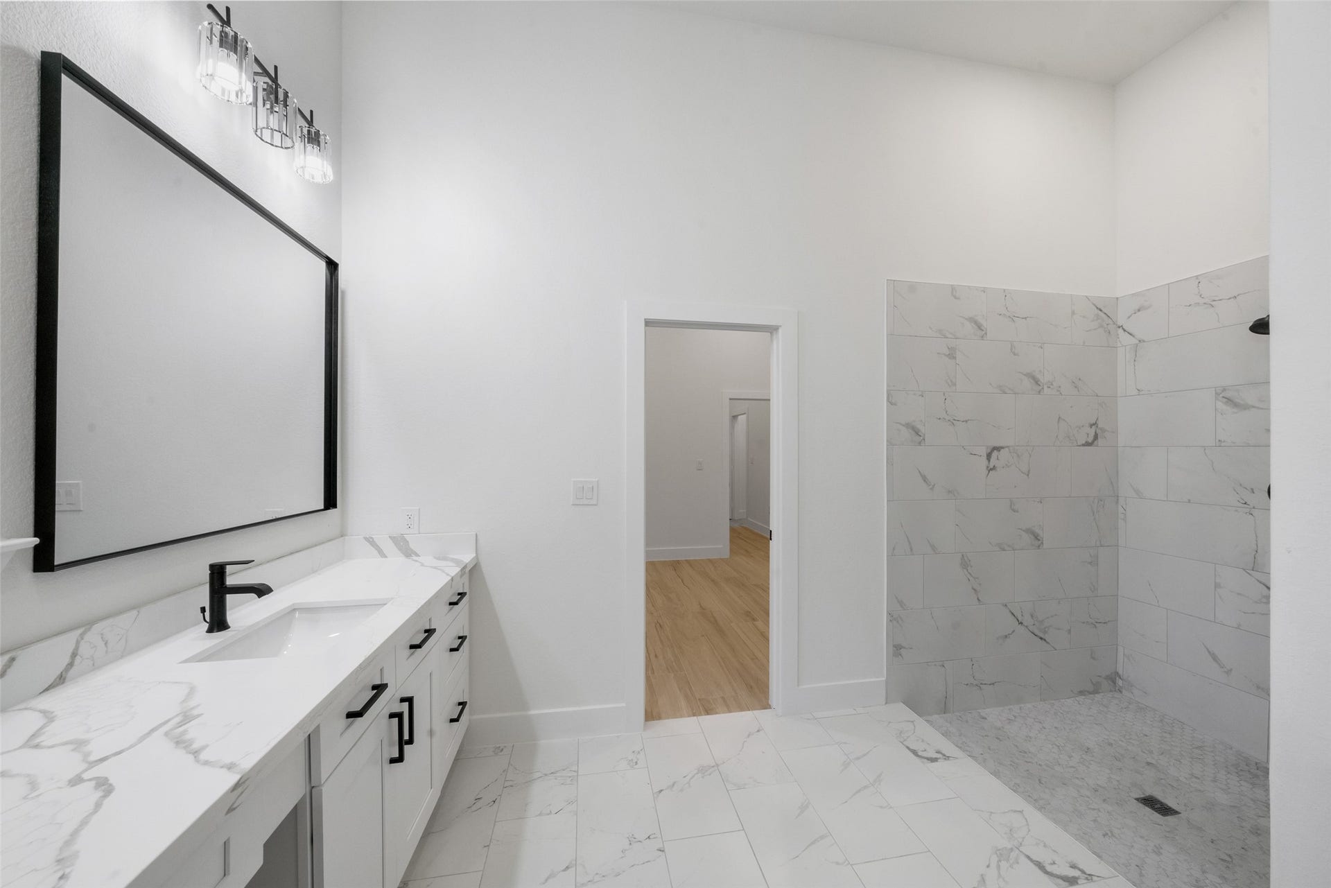 4833 W Fork Boulevard, Conroe, TX 77304 Elegantly designed bathroom showcasing a spacious vanity with marble-look countertops, contemporary black fixtures, and a large framed mirror. Beautifully tiled walk-in shower and sophisticated finishes create a luxurious, spa-inspired retreat.