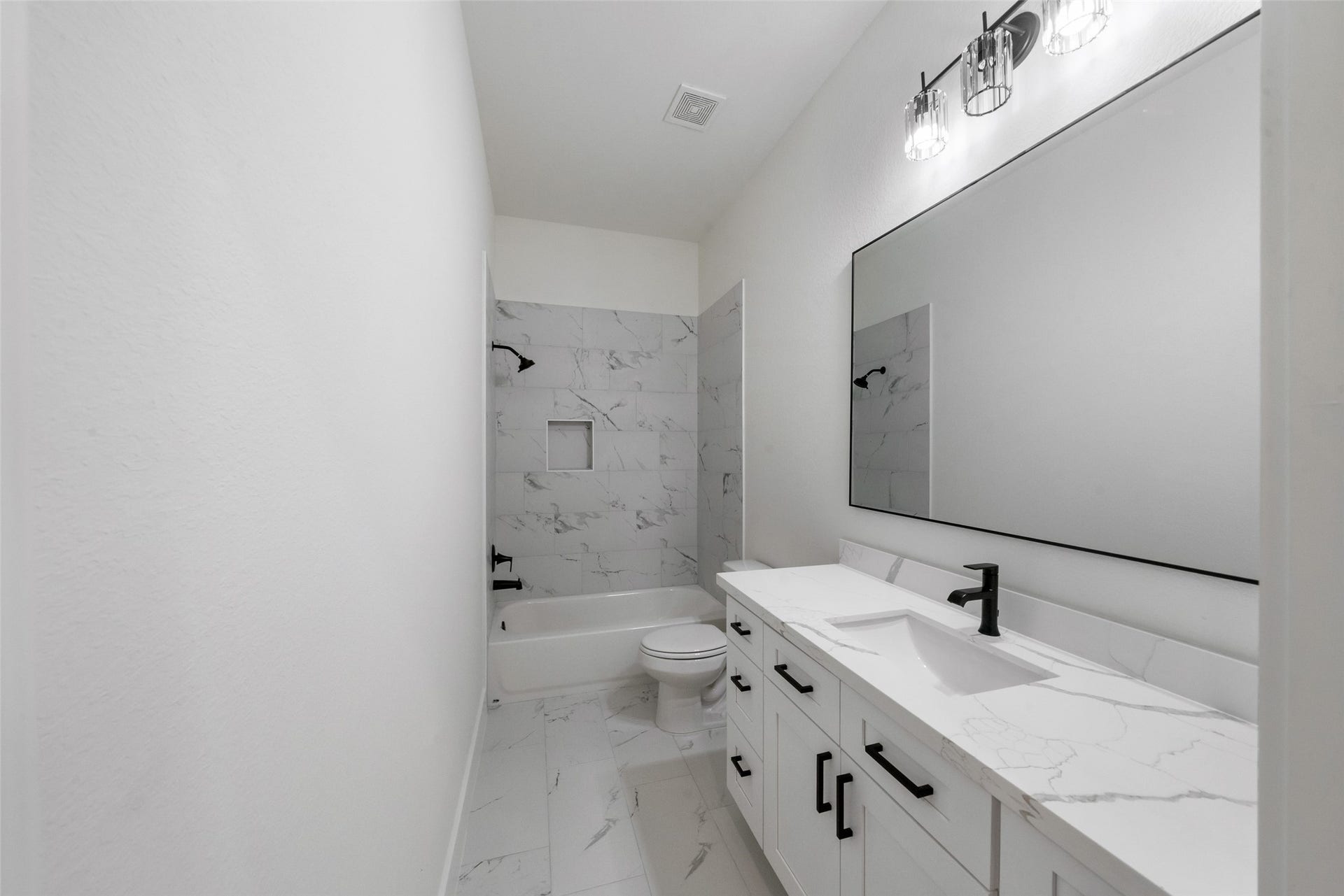 4833 W Fork Boulevard, Conroe, TX 77304 Beautifully finished bathroom featuring marble-look tile, a spacious vanity with sleek black hardware, and contemporary lighting. The shower and tub combination includes elegant tile surrounds and a convenient built-in niche.