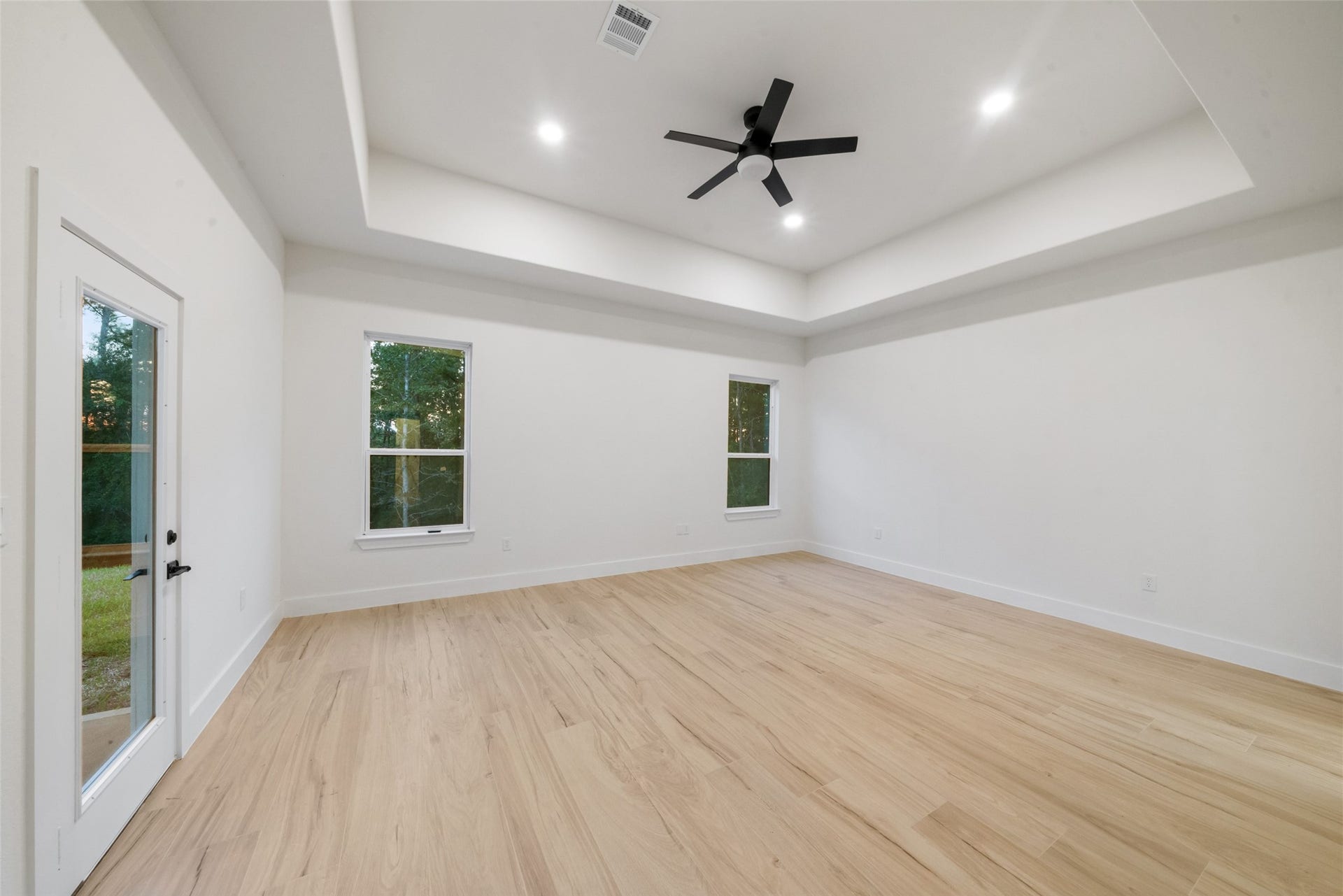 4833 W Fork Boulevard, Conroe, TX 77304 Another view of the spacious primary retreat highlighting its impressive tray ceiling, generous floor space, and beautiful contemporary finishes. Convenient access to the luxurious primary bathroom and private patio adds comfort and functionality.