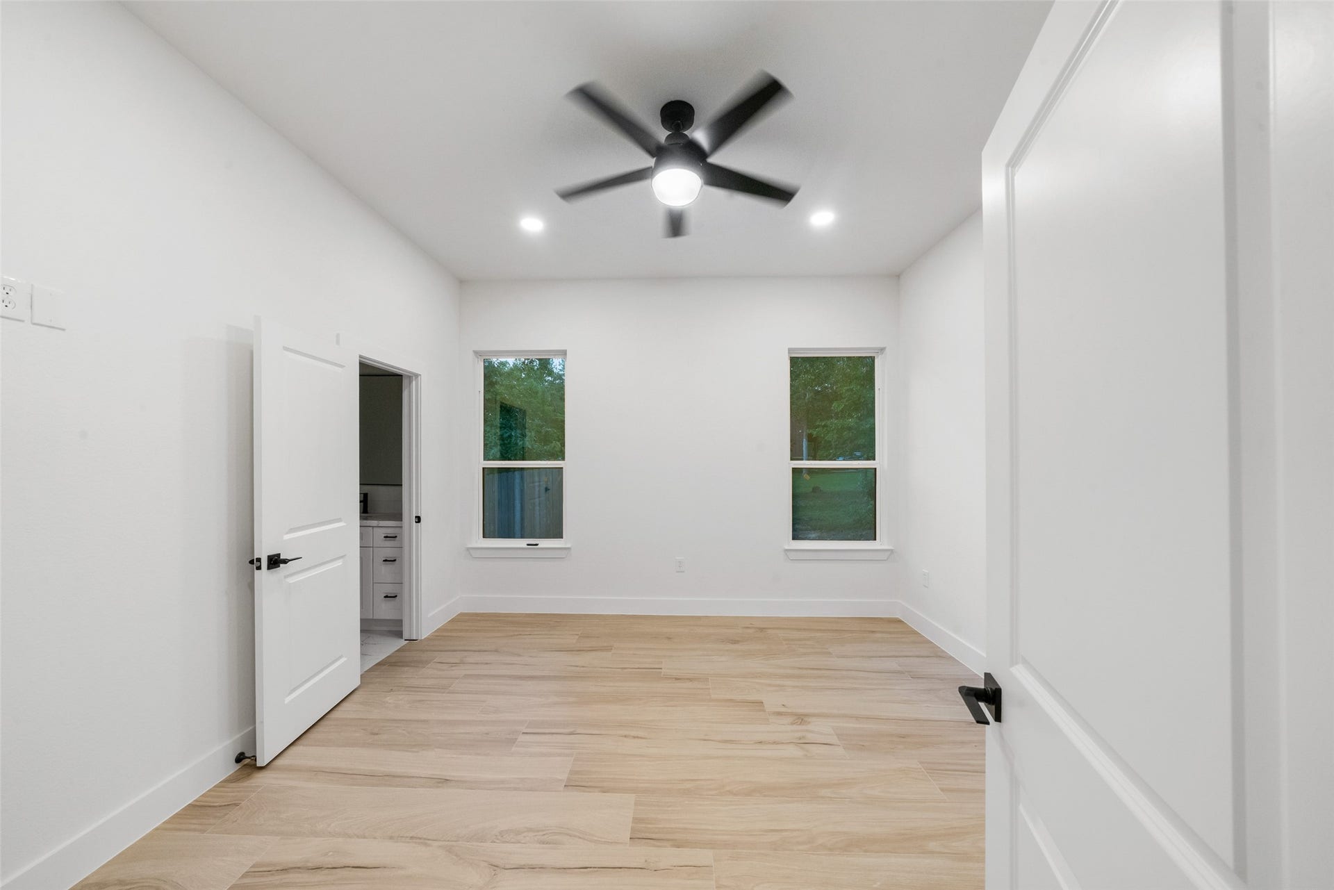 4833 W Fork Boulevard, Conroe, TX 77304 Bright and spacious bedroom featuring beautiful wood-look flooring, recessed lighting, a contemporary ceiling fan, and large windows overlooking the greenery. Neutral finishes and convenient access to an adjoining bathroom complete this inviting space.