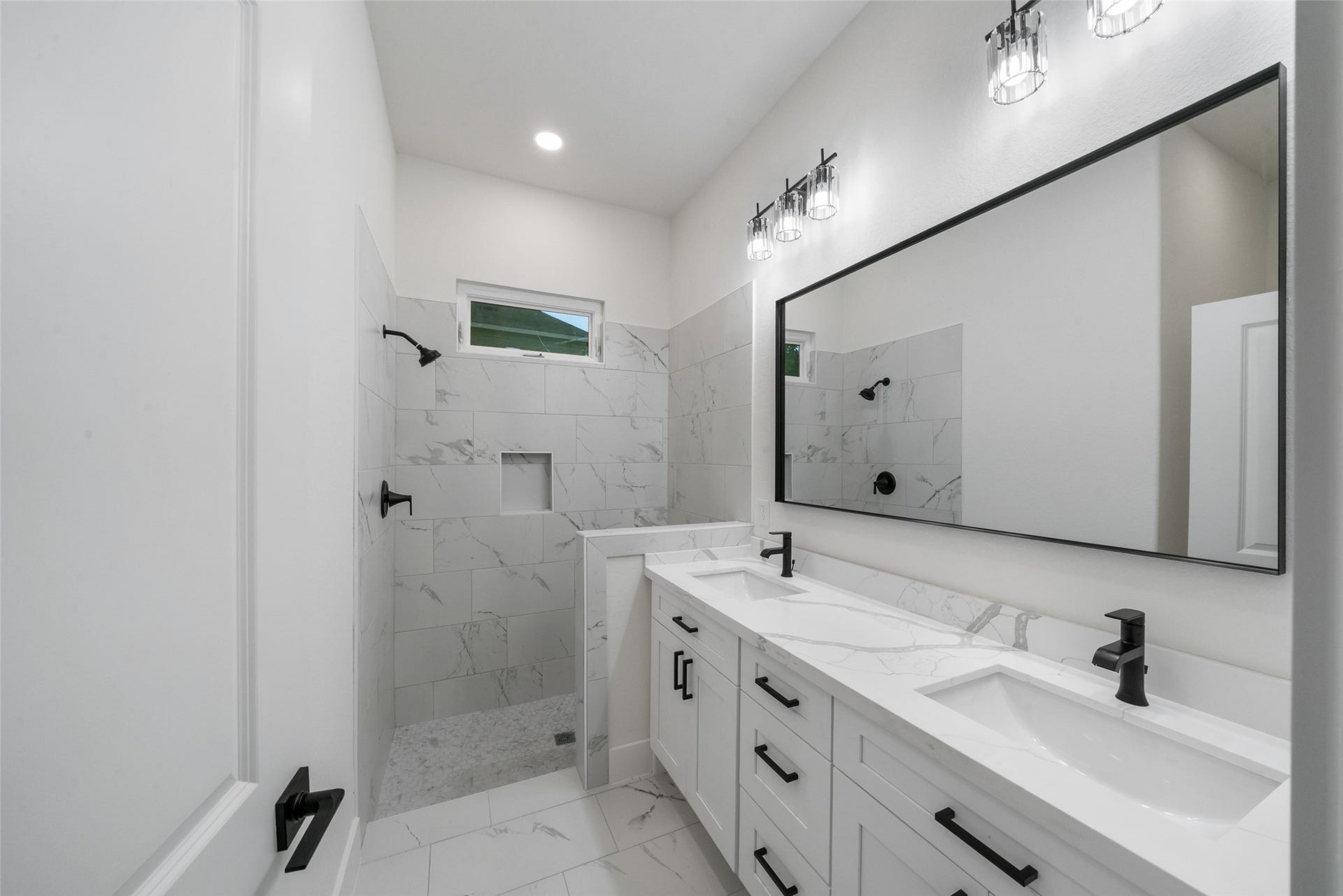 4833 W Fork Boulevard, Conroe, TX 77304 Beautifully appointed bathroom featuring a spacious dual-sink vanity, marble-look countertops, sleek black fixtures, and a tiled walk-in shower with built-in niche. Elegant finishes create a sophisticated, spa-inspired atmosphere.