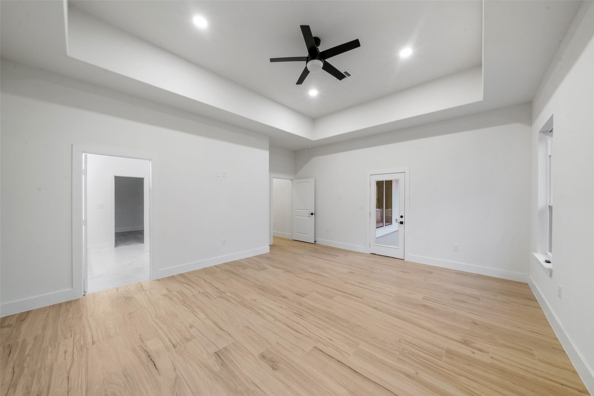 4833 W Fork Boulevard, Conroe, TX 77304 Impressive primary suite featuring soaring tray ceilings, recessed lighting, modern ceiling fan, and beautiful wood-look flooring. An expansive layout provides flexibility for furnishings, with convenient access to the primary bath and covered outdoor living area.
