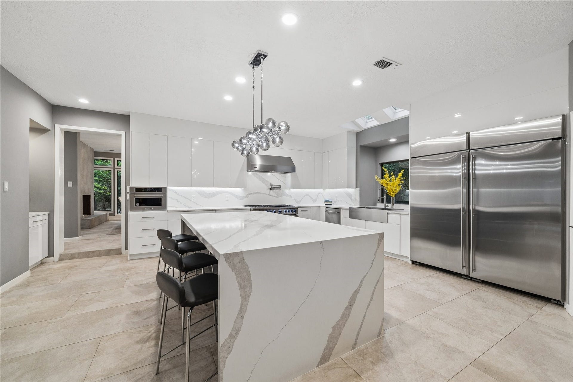 2411 Oakbank Drive, Kingwood, TX 77339 The chef's kitchen features sleek white cabinetry, a large marble island with seating, and stainless steel appliances. The open layout is enhanced by bright lighting and a stylish, contemporary design, perfect for entertaining and everyday living.