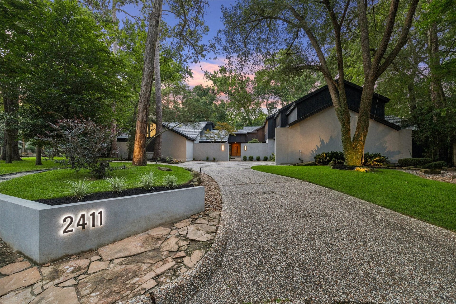 2411 Oakbank Drive, Kingwood, TX 77339 Welcome to Oakbank Estate, nestled among mature trees. The property features a curved driveway leading to the entrance, well-maintained landscaping, and a prominent address marker. The setting is serene and private, ideal for a peaceful living environment.