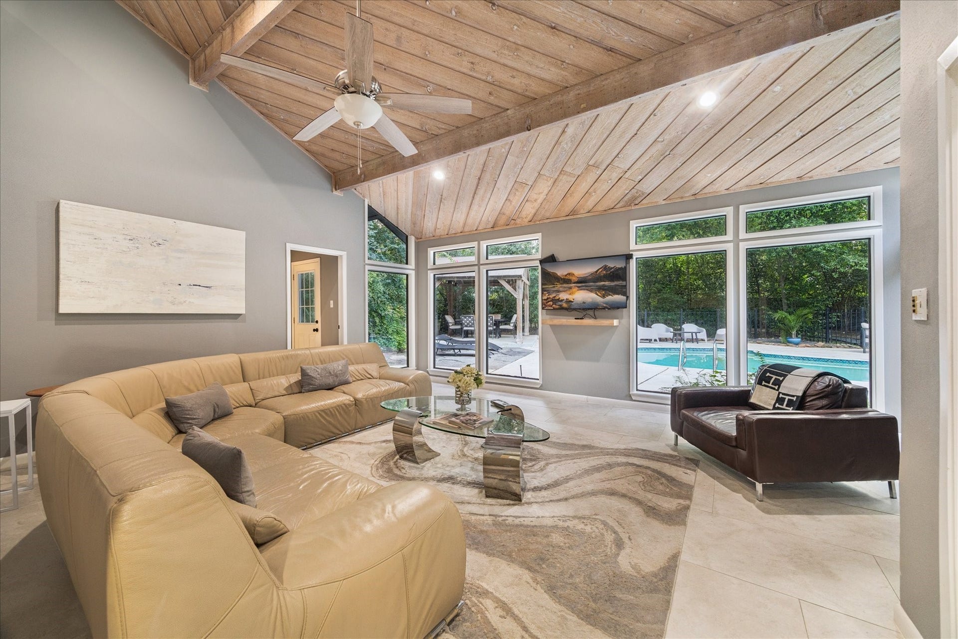 2411 Oakbank Drive, Kingwood, TX 77339 Another spacious living room features a vaulted wooden ceiling and large windows offering a view of the pool and lush greenery outside.