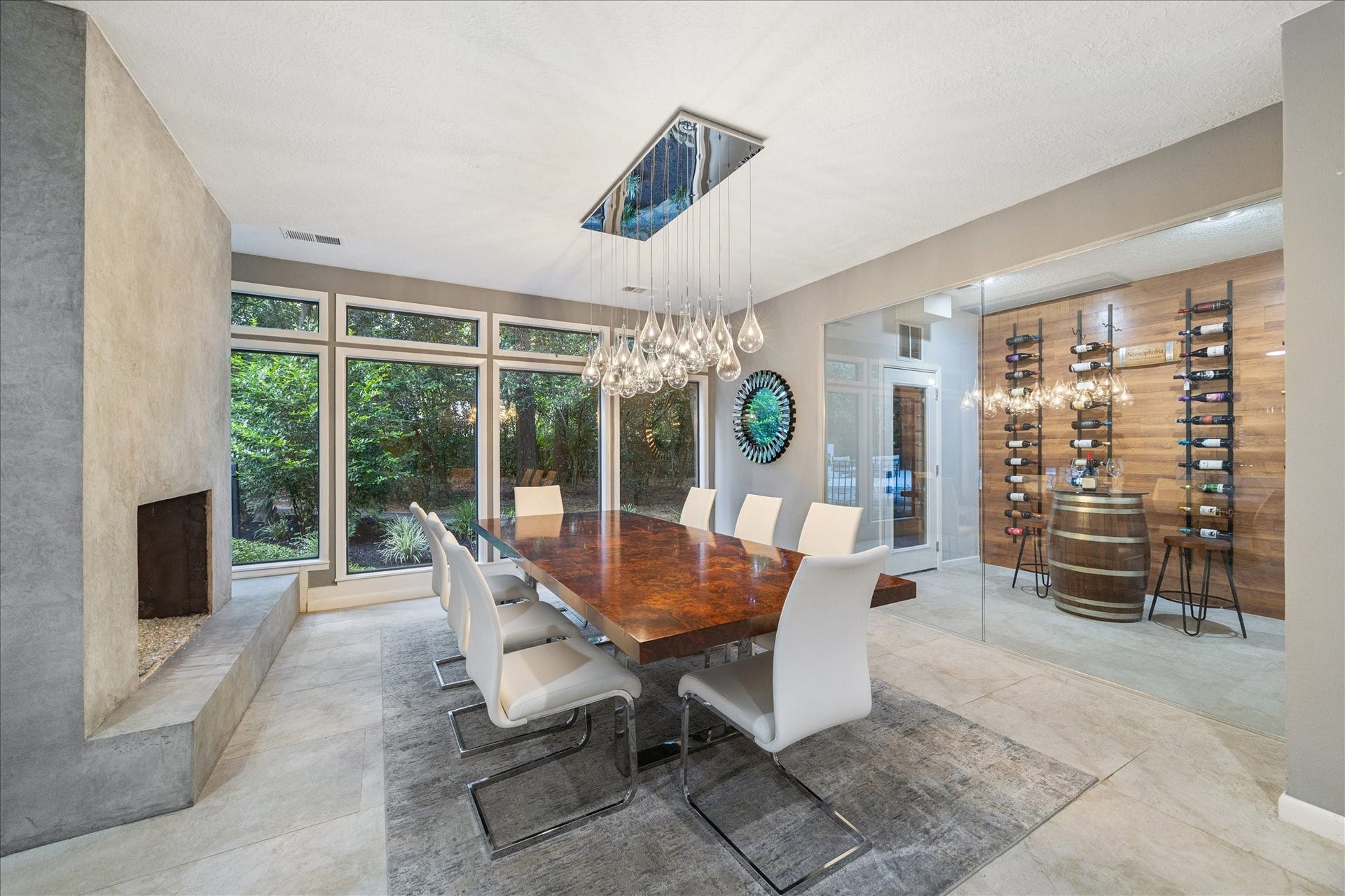 2411 Oakbank Drive, Kingwood, TX 77339 The dining room features a large wooden table with sleek white chairs, a stylish light fixture, and expansive windows offering natural views. The room includes a contemporary fireplace and a glass-enclosed wine display area, creating a luxurious and inviting atmosphere.