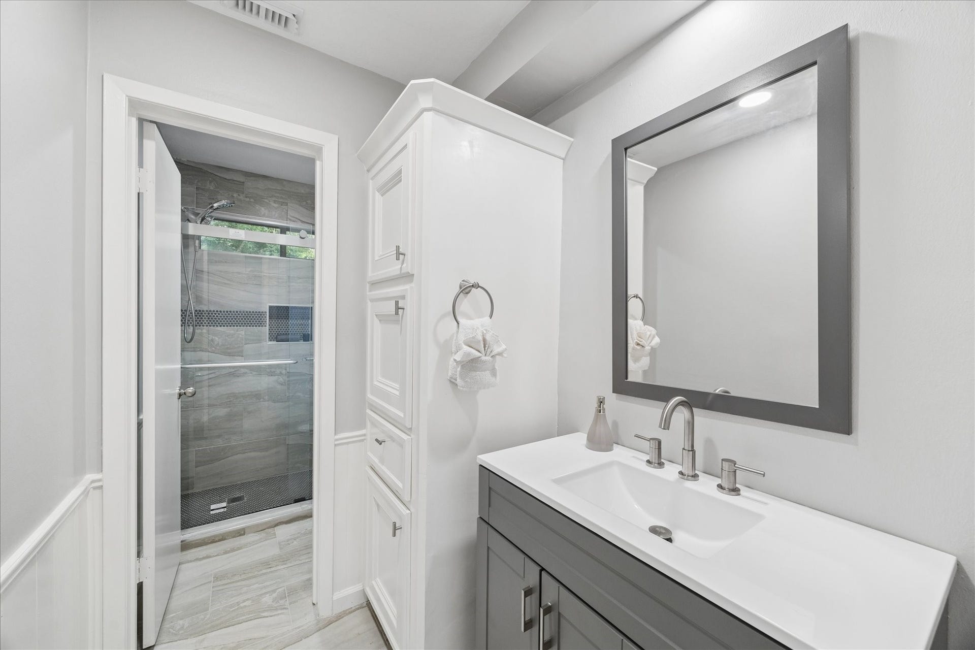 2411 Oakbank Drive, Kingwood, TX 77339 This bathroom features a modern design with a sleek vanity and large mirror. It includes a spacious glass-enclosed shower with stylish tile work. The room offers ample storage and a clean, bright aesthetic.