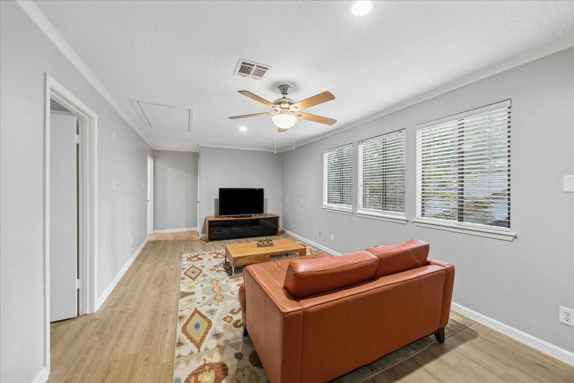 2411 Oakbank Drive, Kingwood, TX 77339 This cozy 2nd-floor living room features a modern ceiling fan, light gray walls, and wood flooring. It includes a comfortable sofa, a stylish area rug, and a TV setup. Large windows provide ample natural light, creating a bright and inviting atmosphere.