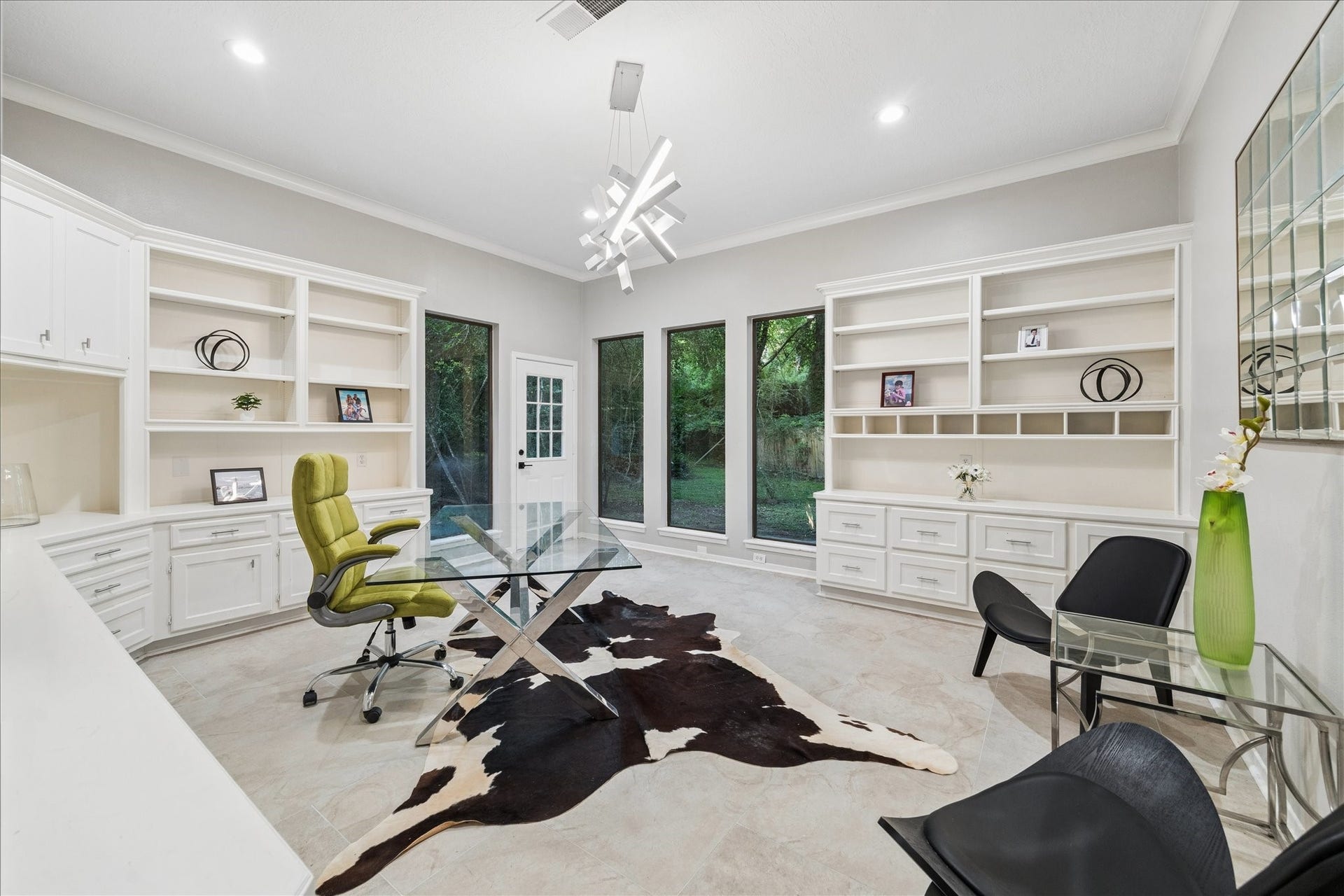 2411 Oakbank Drive, Kingwood, TX 77339 This home office features sleek modern design with ample natural light from large windows. It includes built-in shelving, a stylish glass desk, and contemporary lighting, creating a functional and elegant workspace.