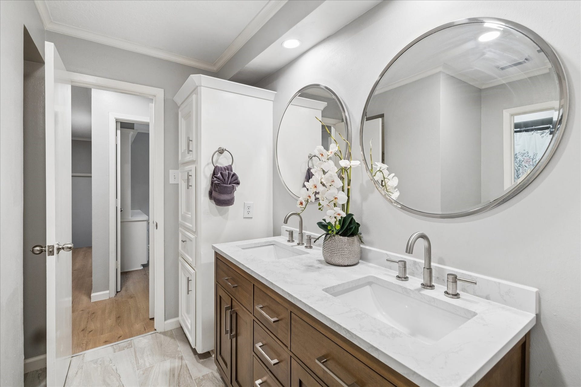 2411 Oakbank Drive, Kingwood, TX 77339 This bathroom features a modern double vanity with a sleek marble countertop, large round mirrors, and contemporary fixtures. It has ample storage with a tall cabinet and stylish wood cabinetry, set against a neutral color palette.