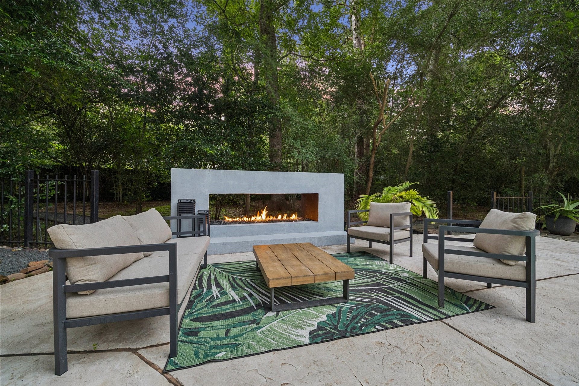 2411 Oakbank Drive, Kingwood, TX 77339 This inviting outdoor space features a modern fire pit surrounded by comfortable seating, set on a stylish patio with a lush, wooded backdrop. Perfect for relaxing or entertaining.